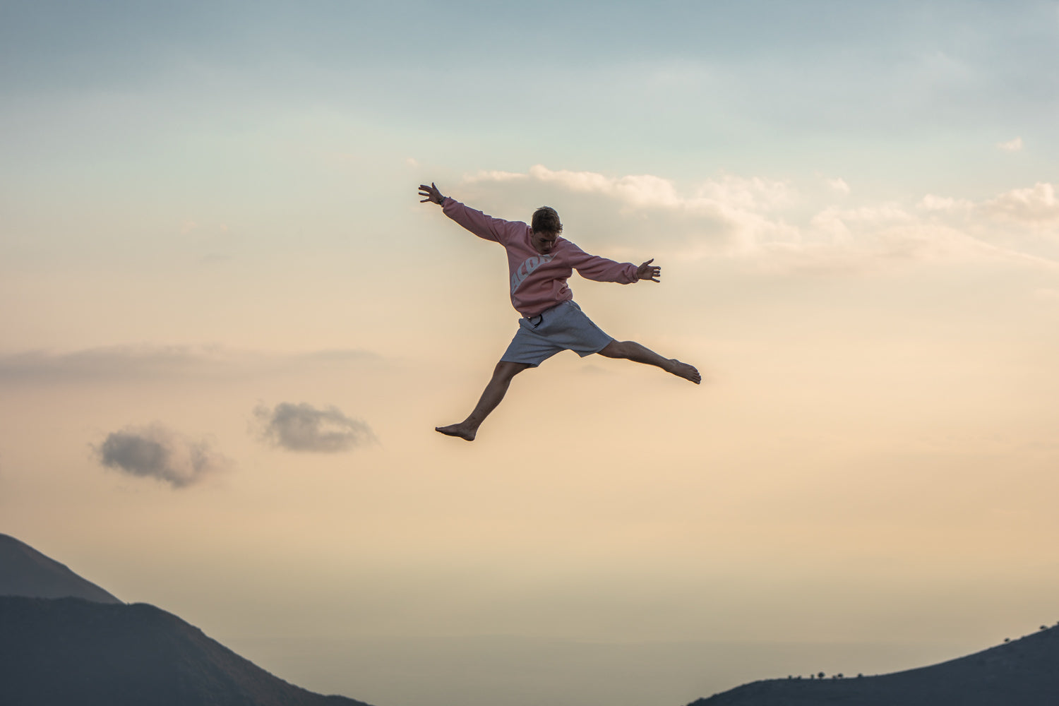 Trampoline leaper wearing a pink Acon sweatshirt in a Grecian landscape.