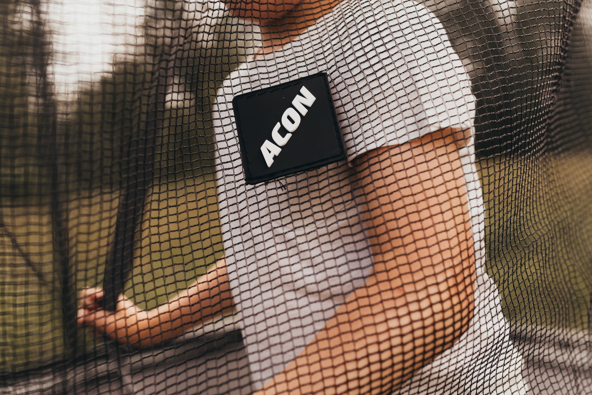 A kid in a white t-shirt behind the trampoline's safety net that has ACON logo on it 