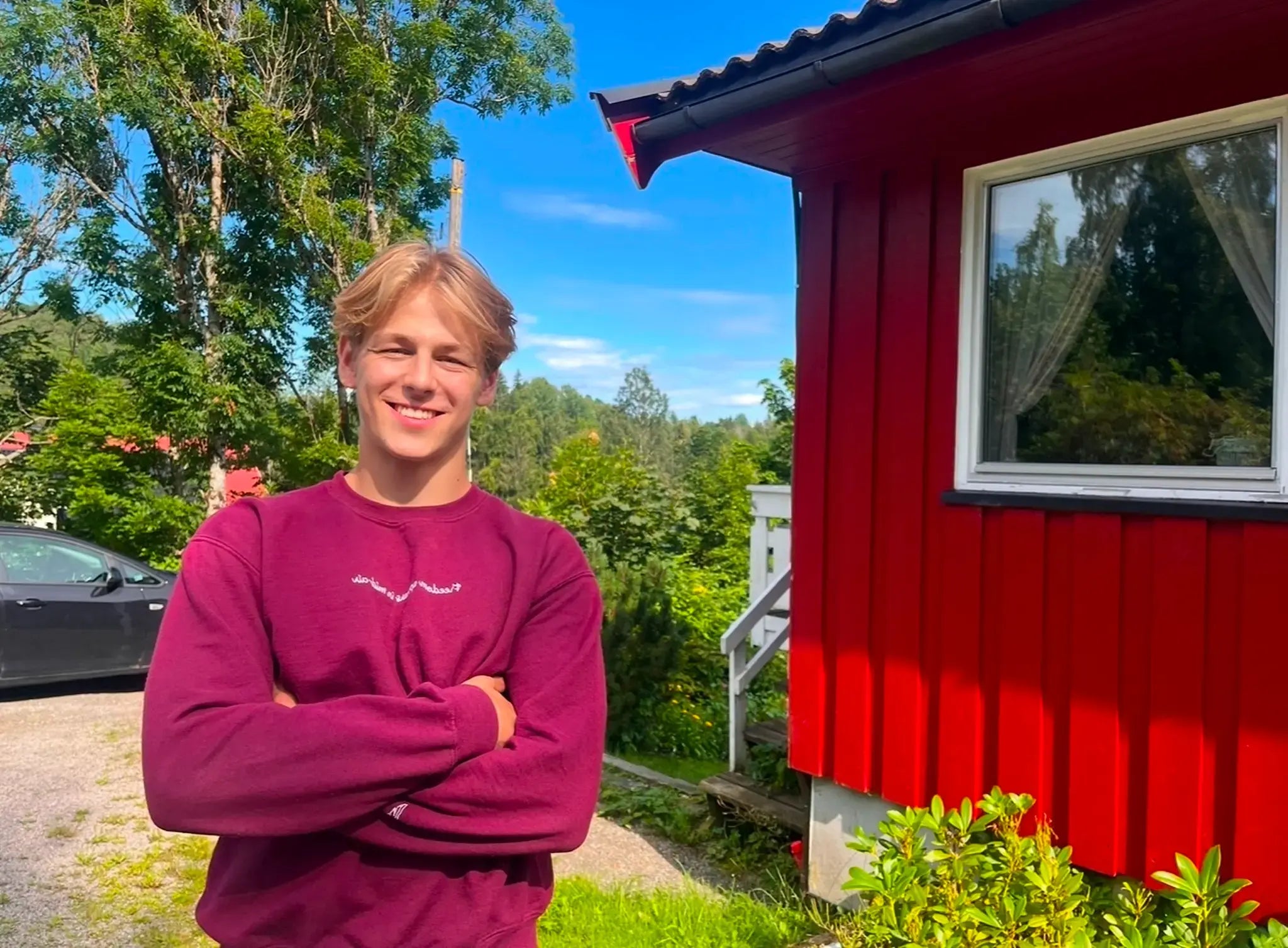 Trampoline athlete Sebastian Fuglestad smiling at the camera in the yard of a red house.