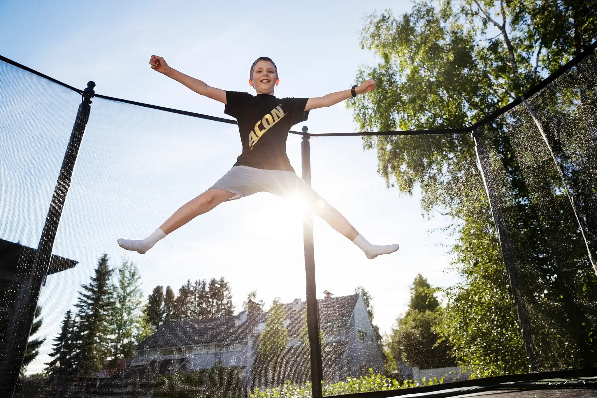 Happy boy doing x-jump on an Acon trampoline while wearing Acon t-shirt.
