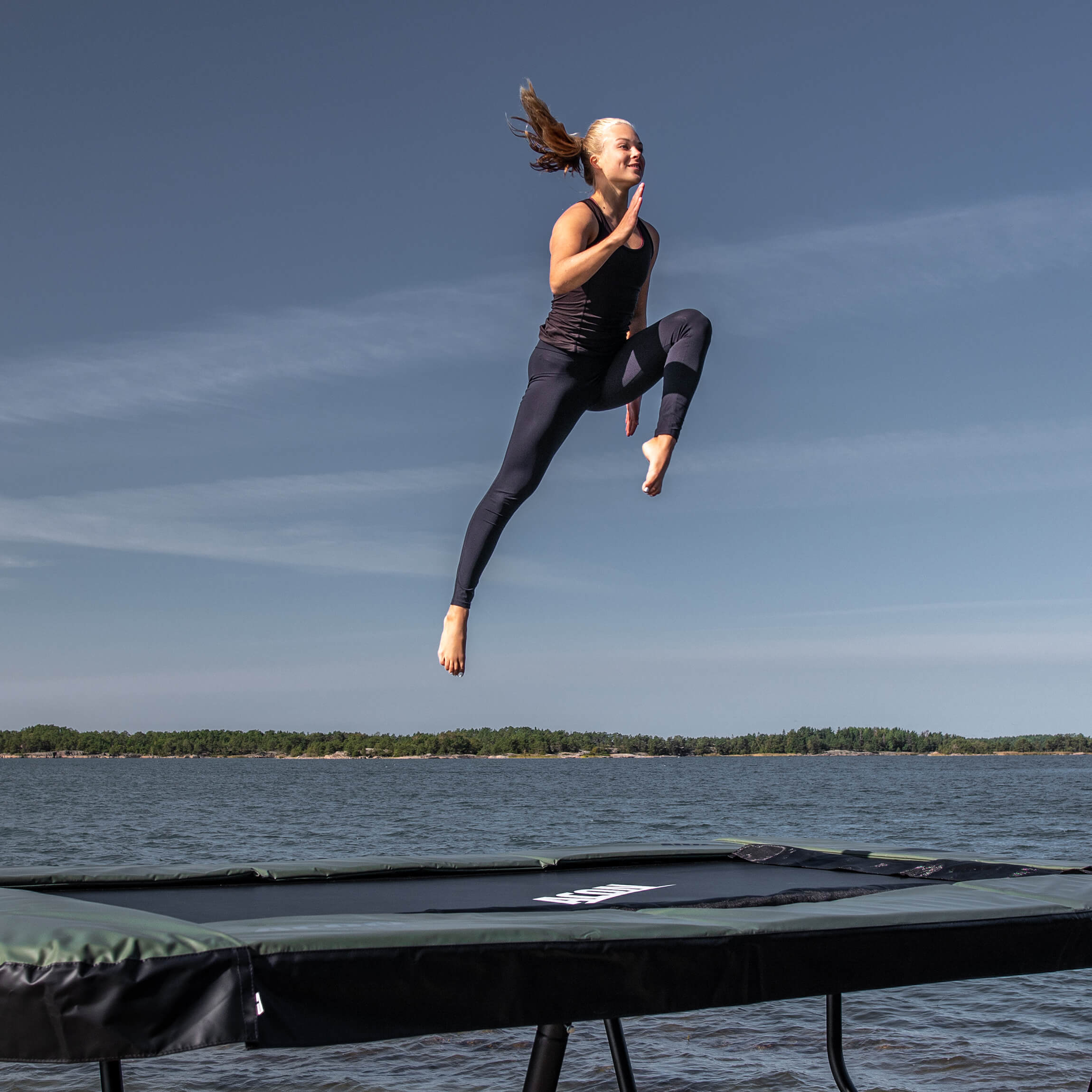 A gymnast jumps on an Acon 13 HD trampoline in an archipelago landscape.