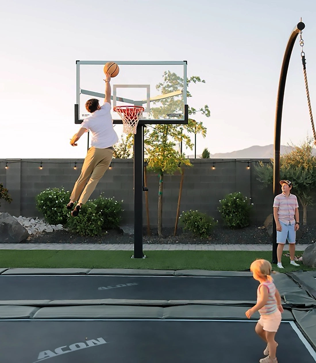 A man jumpping on an in-ground assembled Acon HD trampoline and throws a basketball.