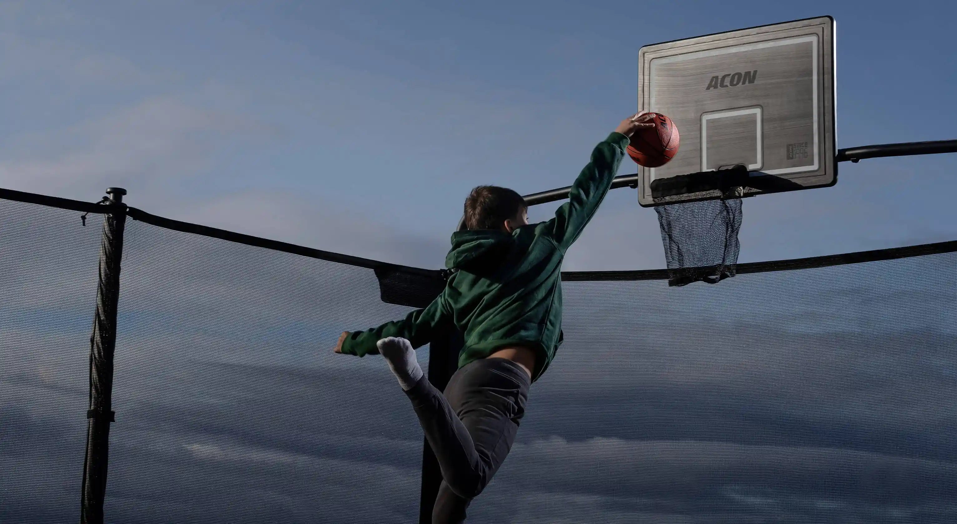 A boy throws a basketball into the basketball hoop of the trampoline.