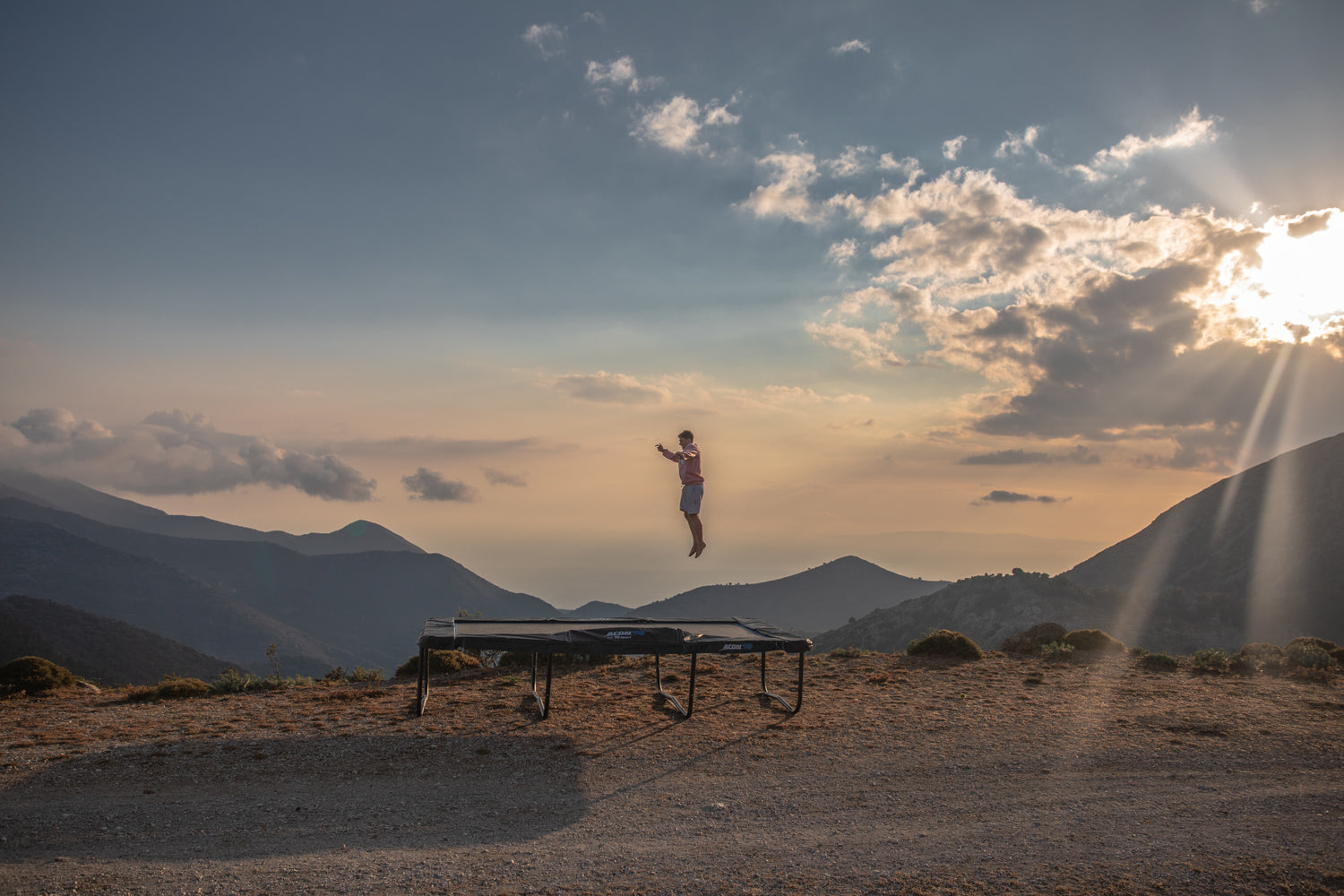 A guy jumping on an ACON rectangular trampoline in a desert