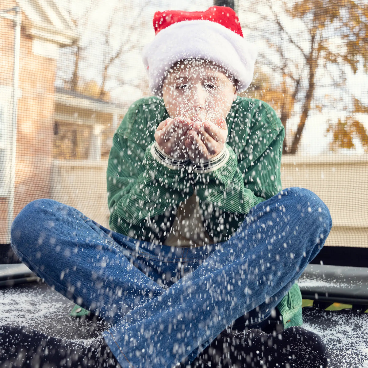 Child wearing a Santa hat blowing snow while sitting on a Acon trampoline.