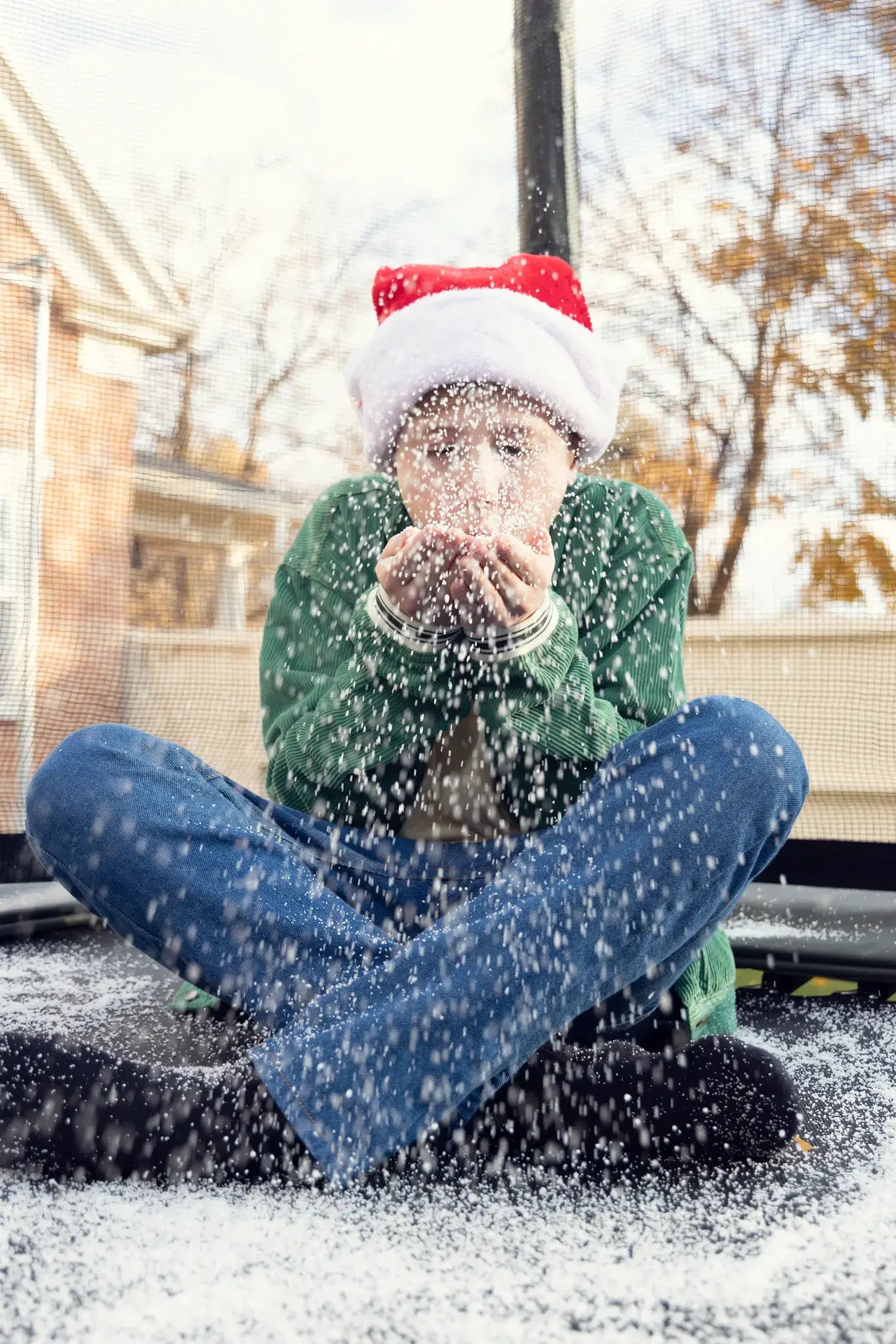 Child wearing a Santa hat blowing snow while sitting on a Acon trampoline.