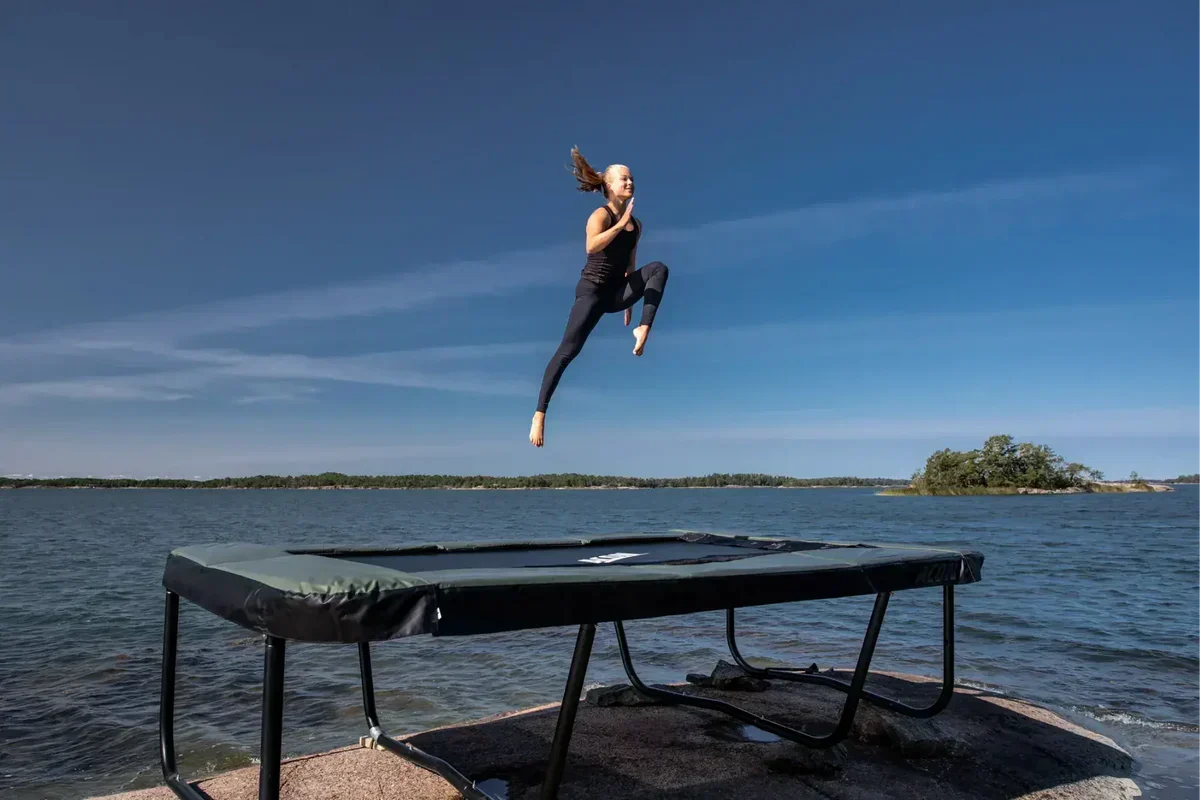 Girl jumping on an Acon rectangular trampoline in front of a lake.