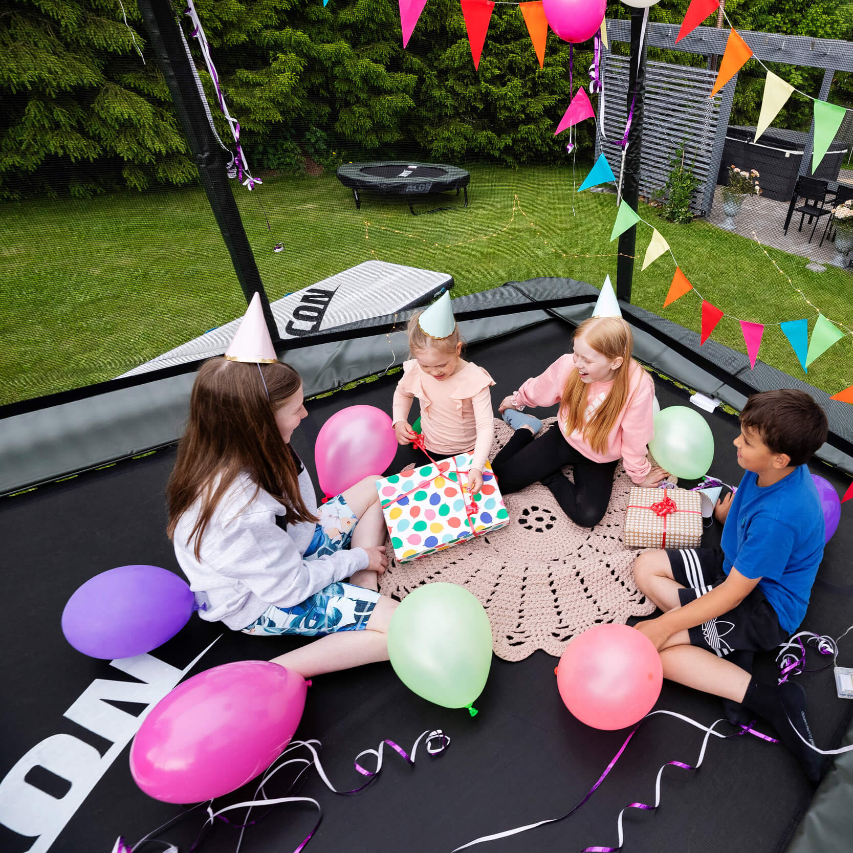 4 children celebrate a birthday party on a trampoline decorated with balloons and serpentine.