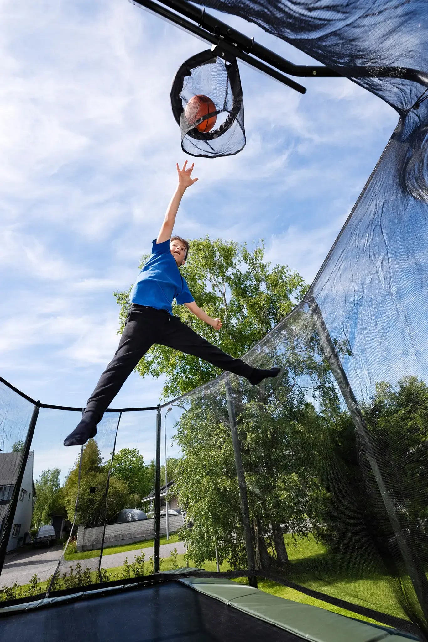 Boy jumping on a Acon trampoline and shooting a basketball into a hoop outdoors.