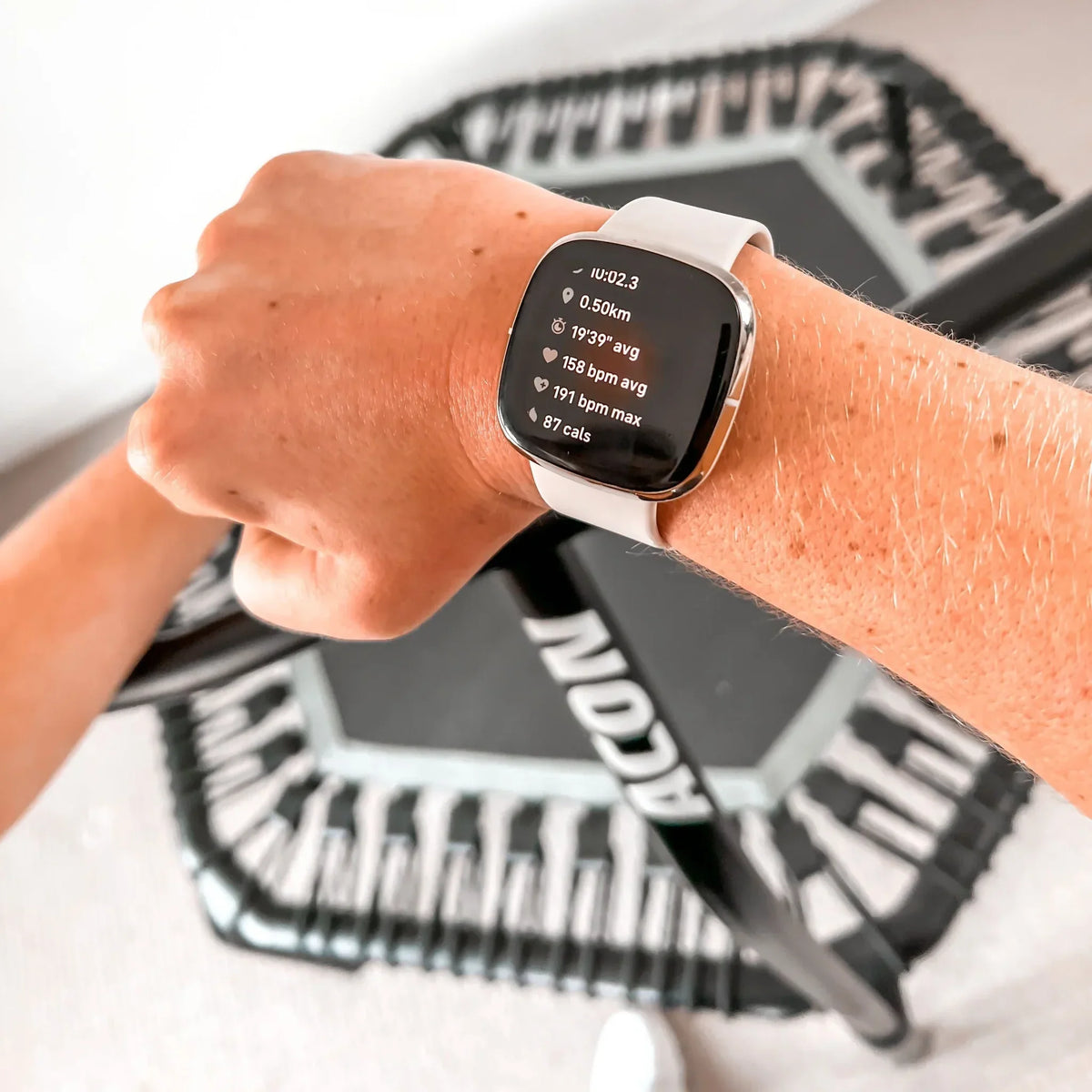 A closeup of a sports watch with an ACON rebounder trampoline in the background.