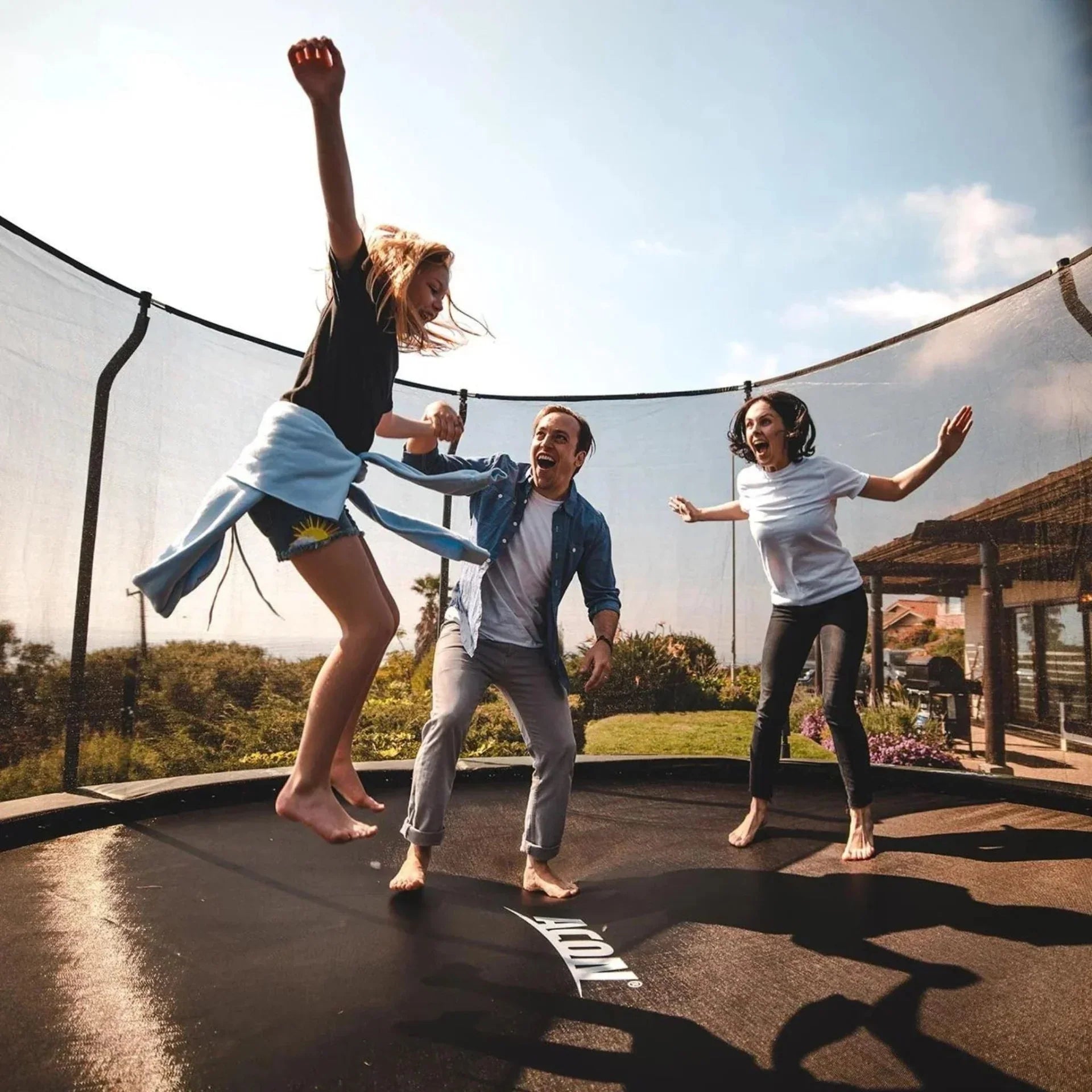 Family on an Acon trampoline, with the girl jumping and parents standing.