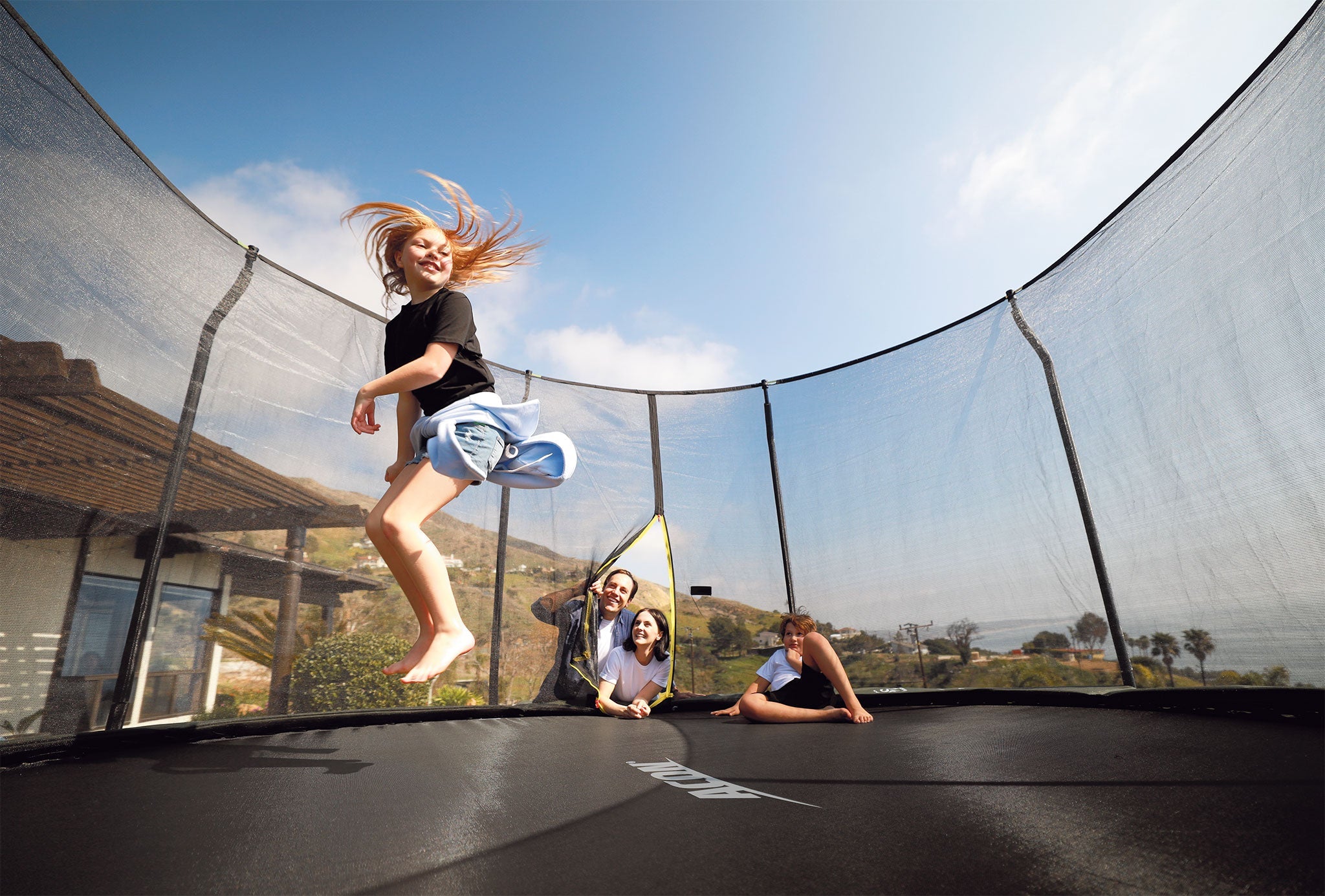 Family watching a girl jumping on one of ACONs safest trampoline with premium enclosure.