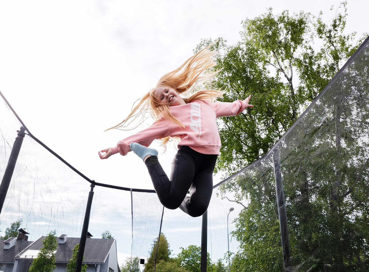 Girl wearing a pink Acon  sweater and jumps on Acon trampoline