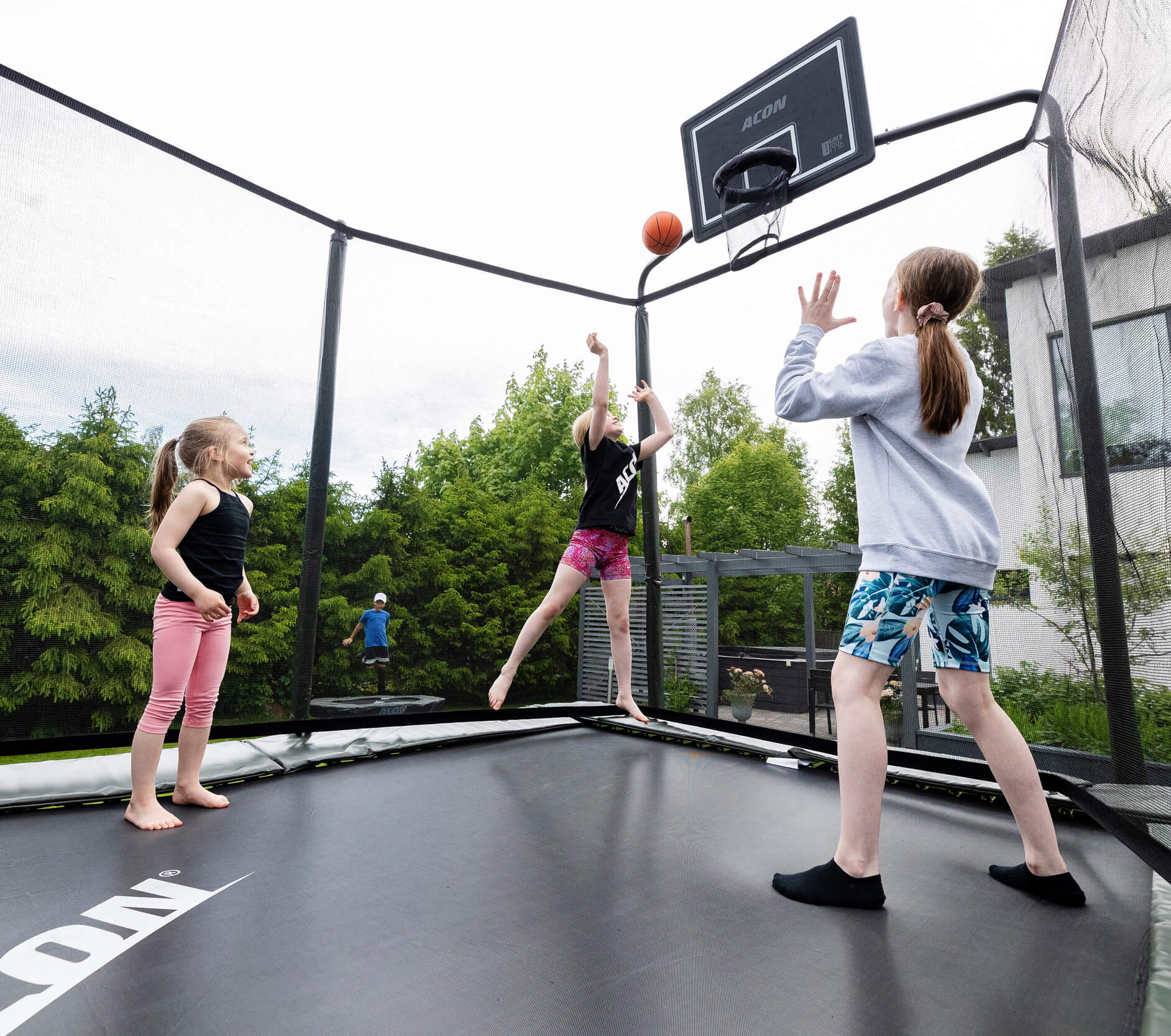 3 girls playing basketball on a trampoline with safety net.
