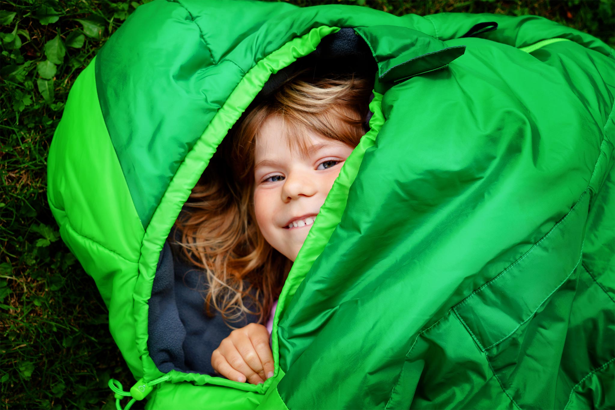 A child peeking and smiling inside the sleeping bag