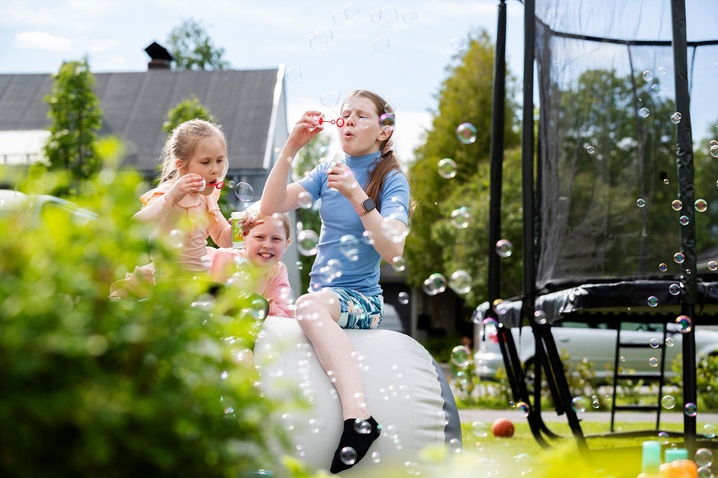 Kids blowing soap bubbles on an Airroll. Behind there is a garden and a trampoline.