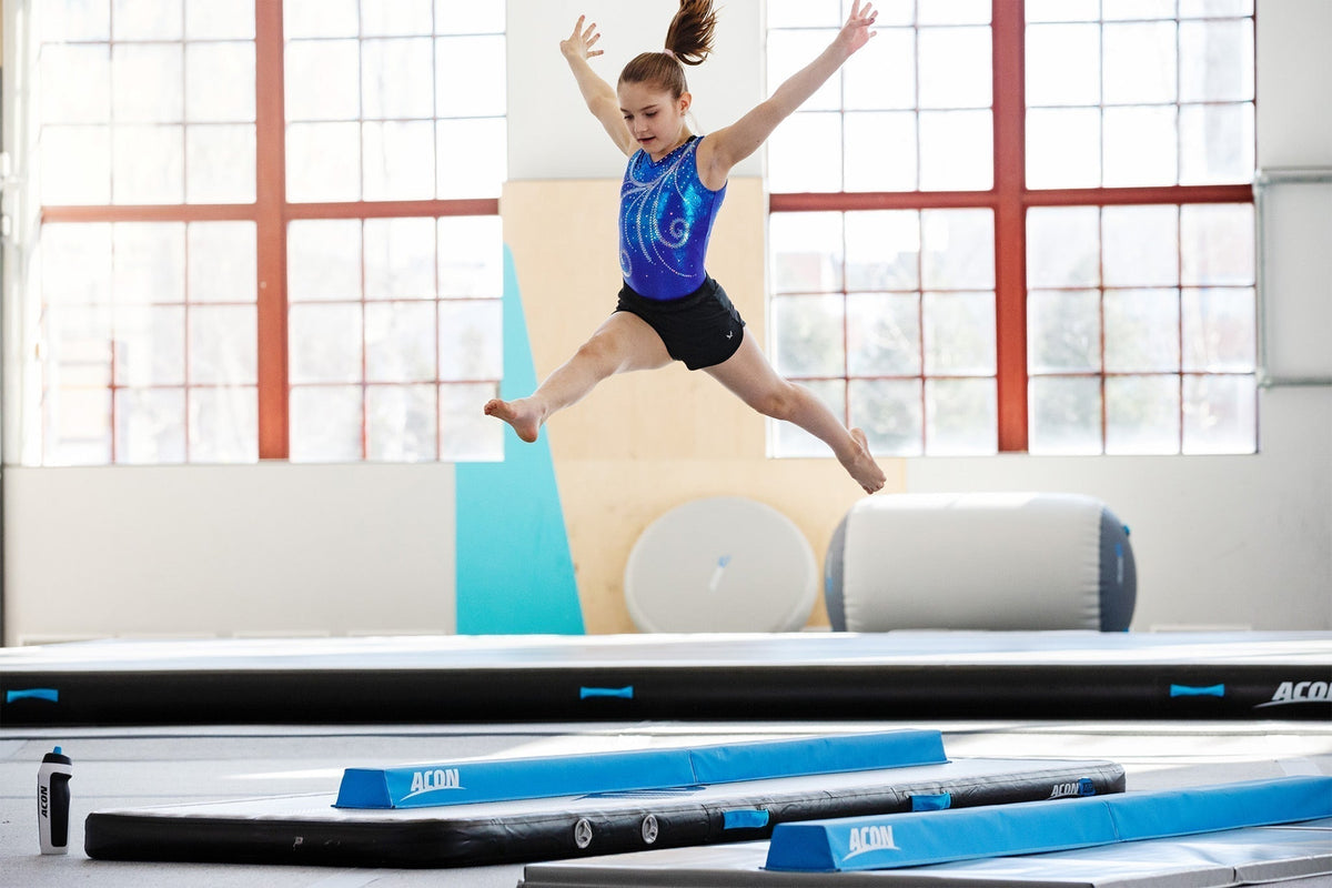 Girl doing a split leap on an ACON gymnastics mat with airtracks and airrolls in the background.