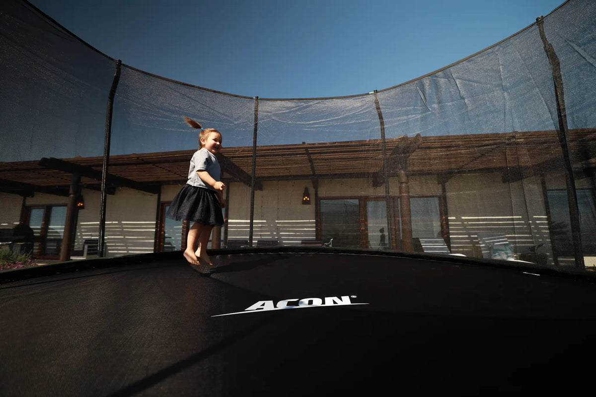 Young girl jumping on a round Acon trampoline with safety net. 