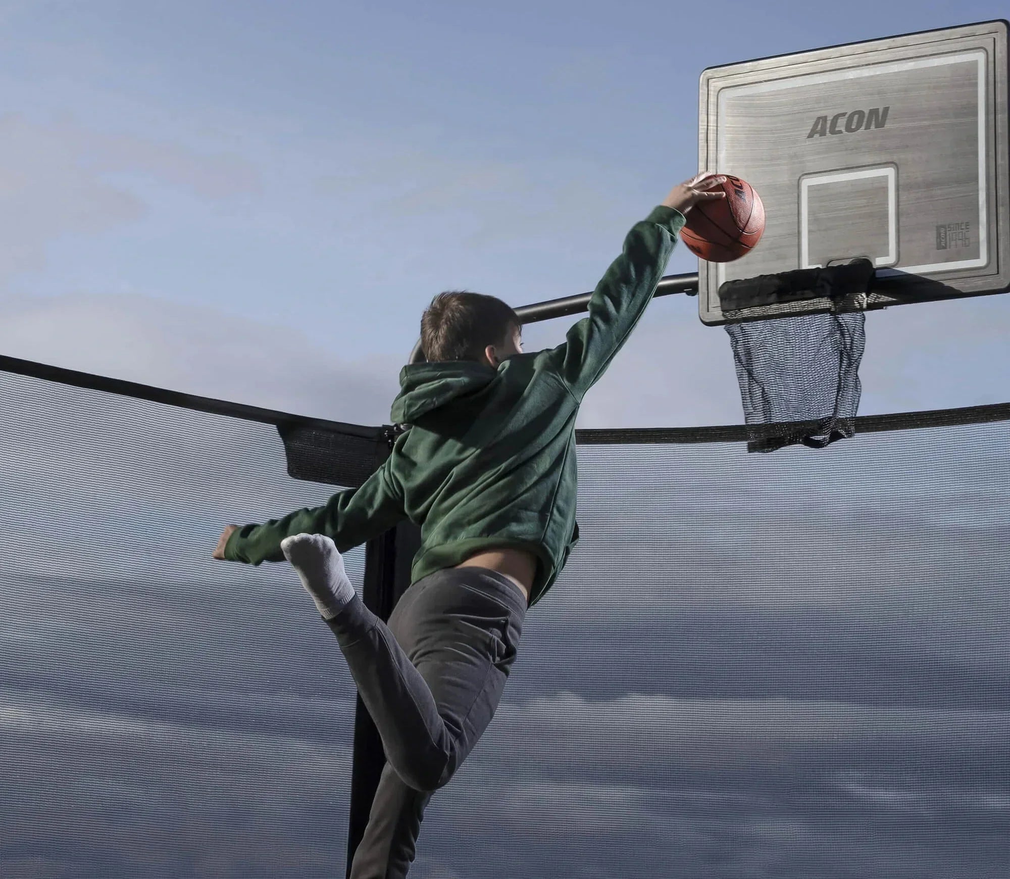The boy throws the ball into the trampoline basketball hoop.