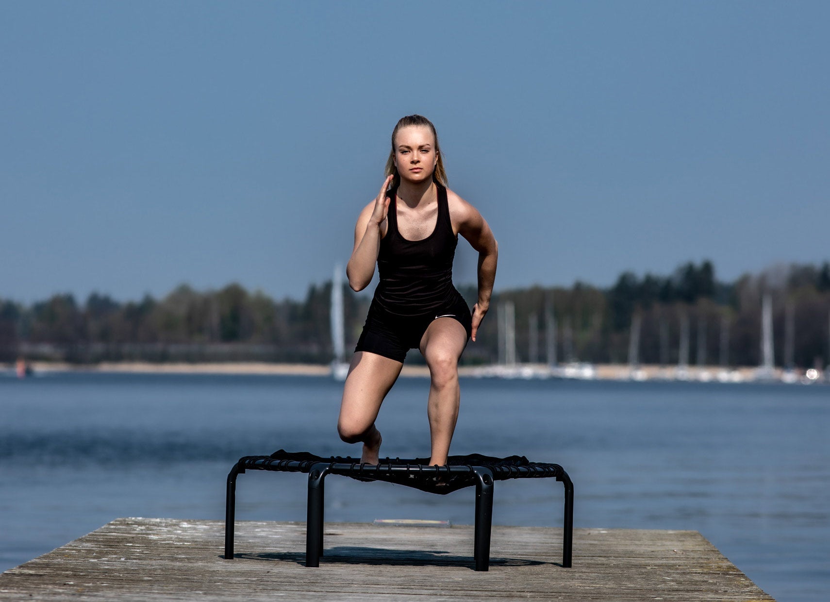 A young woman doing lunges on a black fitness trampoline