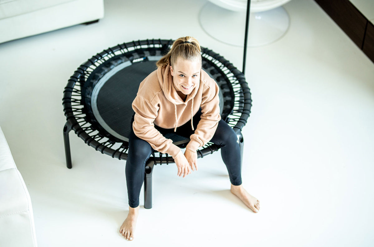 Fitness trampoline and a woman. The woman sits on the black ACON fitness trampoline.