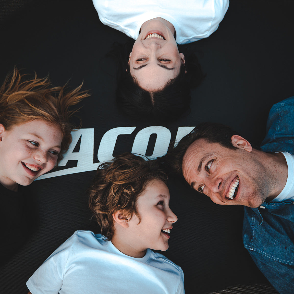 A closeup photo of a family of four smiling while laying on an ACON trampoline