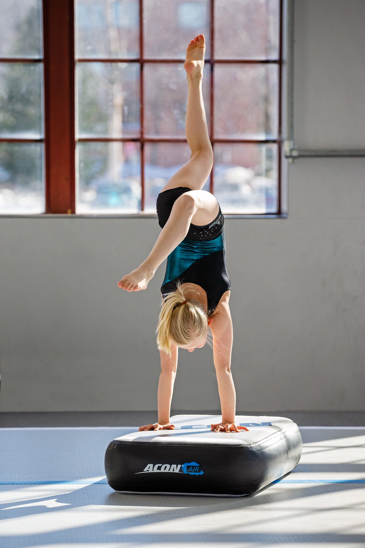A girl doing a handstand on an airblock at the gym