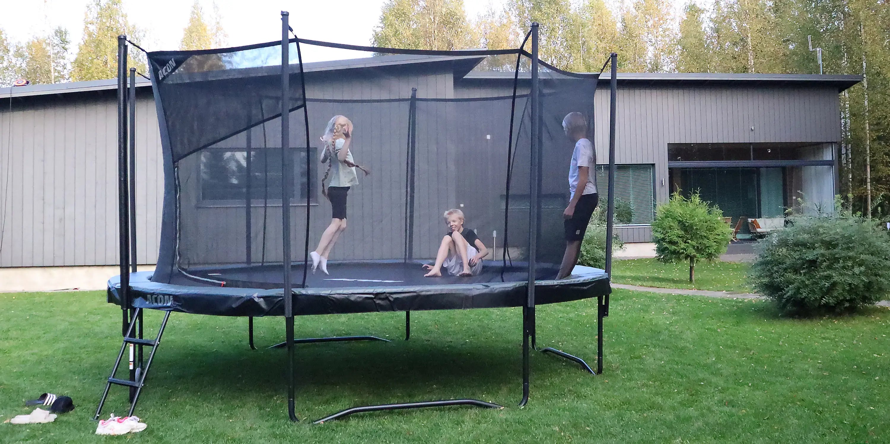 Three children jumping on an Acon 4.3m round trampoline in a sunny backyard, showing how big a 14ft trampoline is.