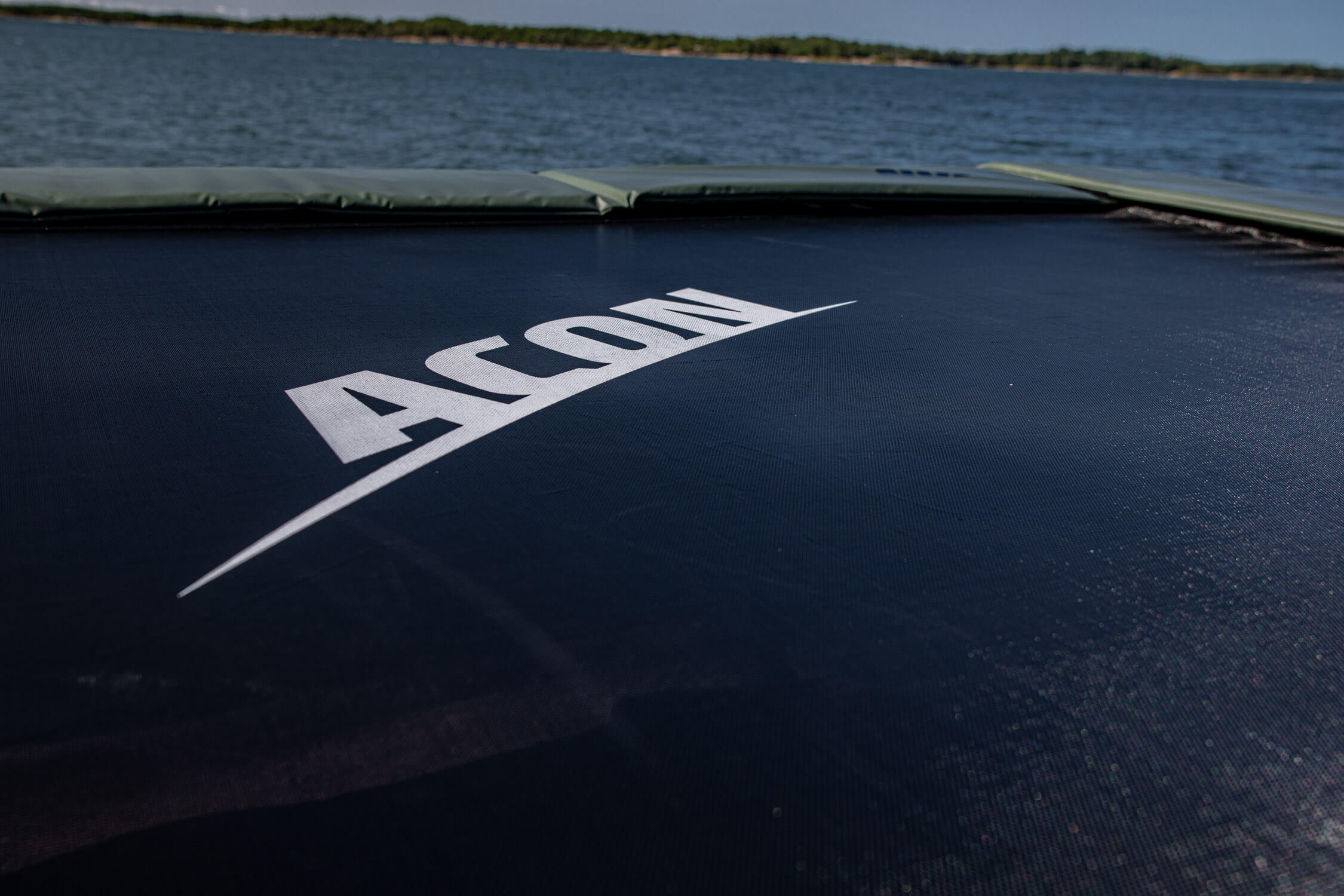 A closeup of trampoline with a focus on the black trampoline mat with white ACON logo.