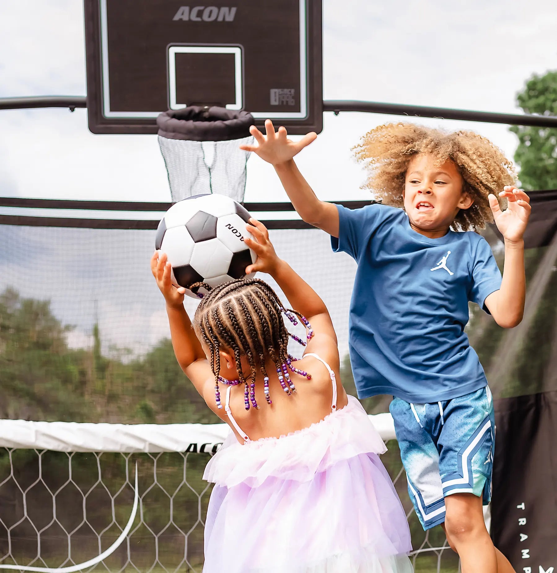 Two children playing with a soccer ball on an Acon X trampoline.