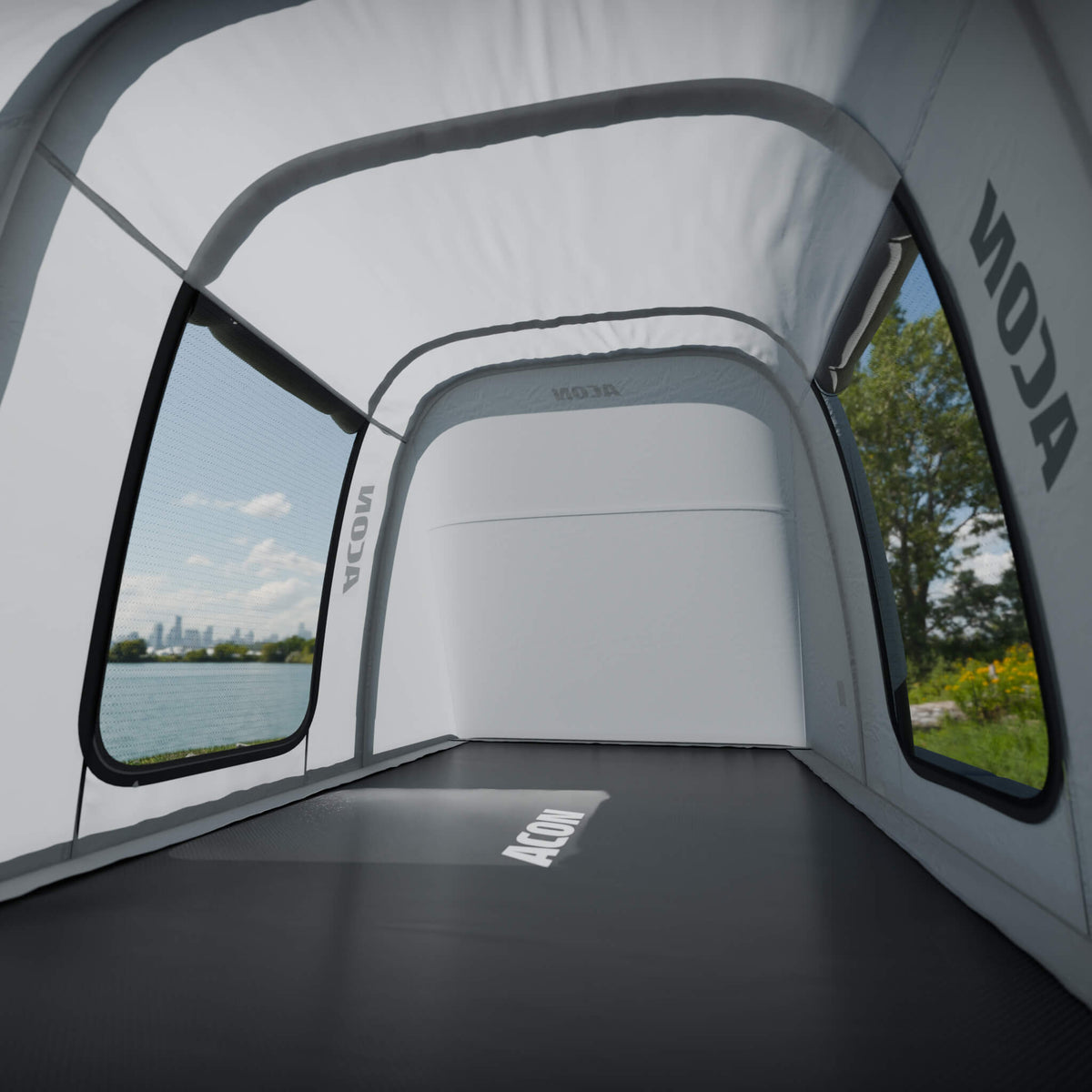 Interior view from inside the Acon Trampoline Tent, showing the spacious inside. The tent features large mesh windows offering a clear view of a sunny park landscape outside, creating an airy and open feel.