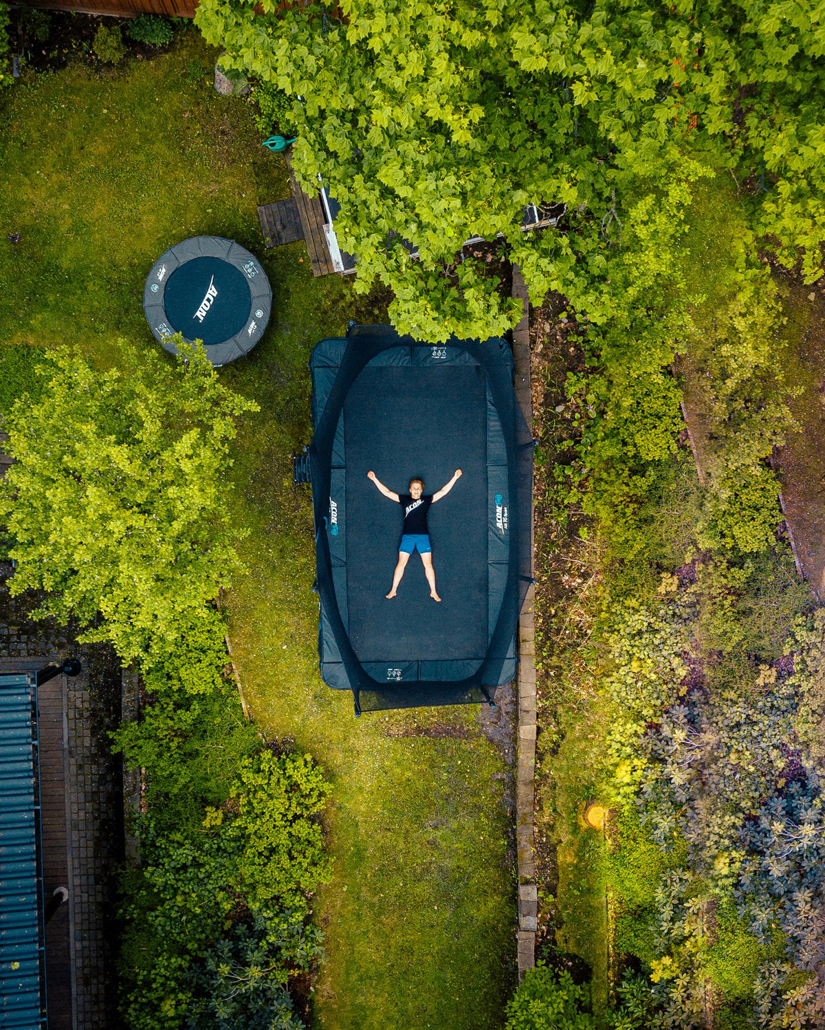 A boy lying on Acon 16 HD trampoline in a backyard, seen above
