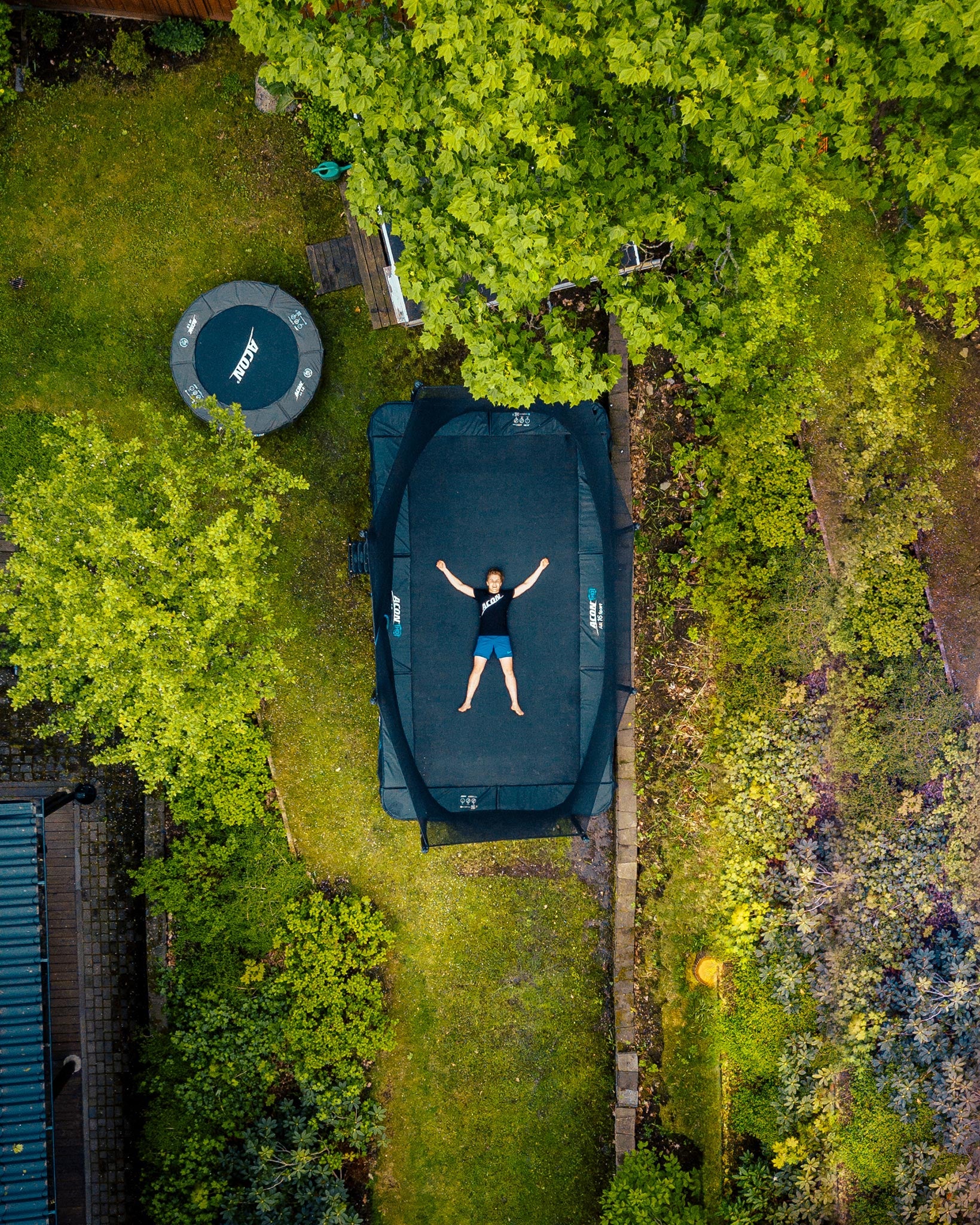 A boy lying on Acon 16 HD trampoline in a backyard, seen above