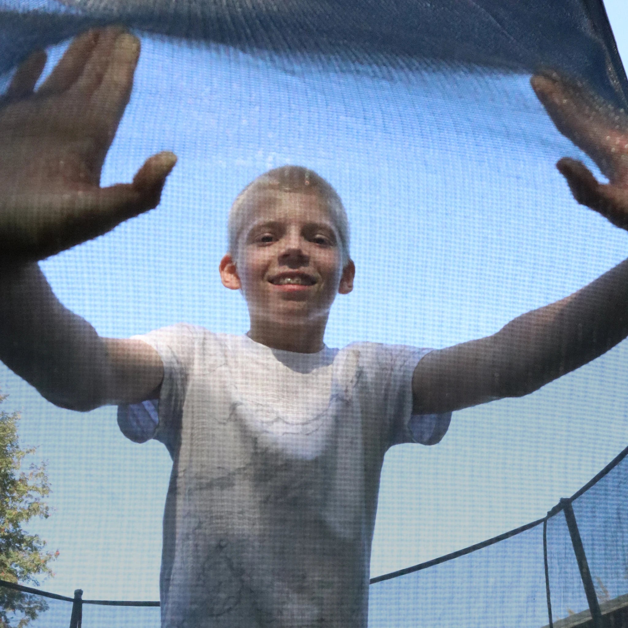 A boy leans on the Acon Air trampoline safety net with his hands.