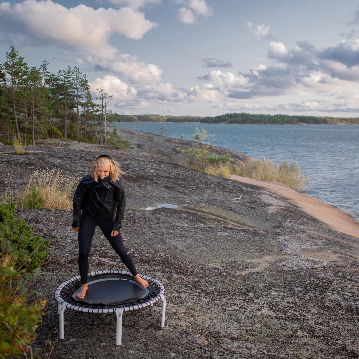 A woman wearing a windbreaker is standing on an Acon rebounder in a northern coastal landscape.