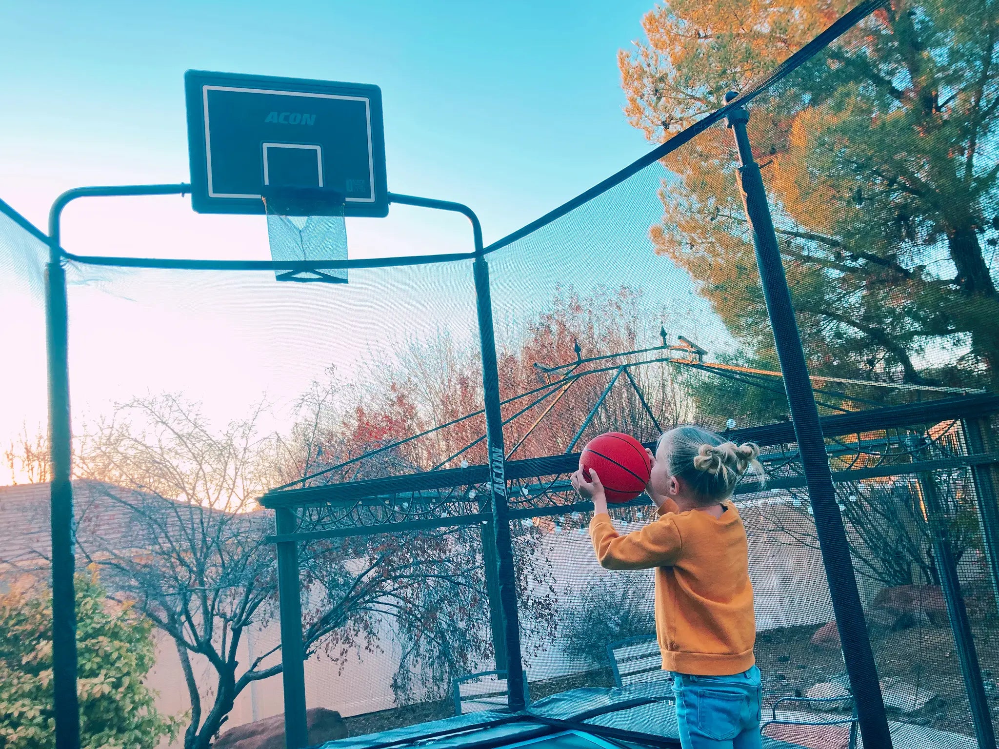 A small girl attempting to throw a basketball on a trampoline.