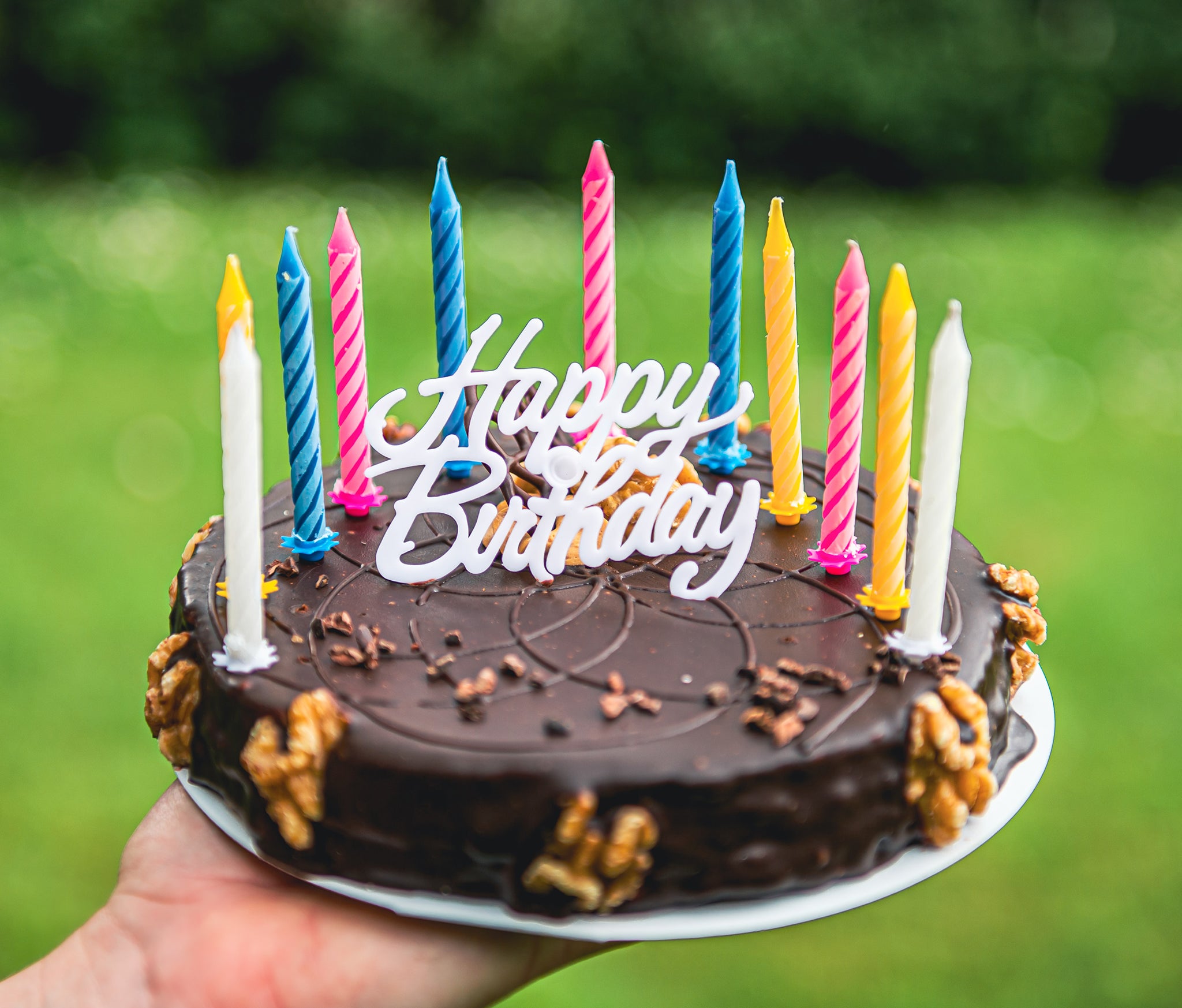 A hand holding a chocolate frosted birthday cake with candles.