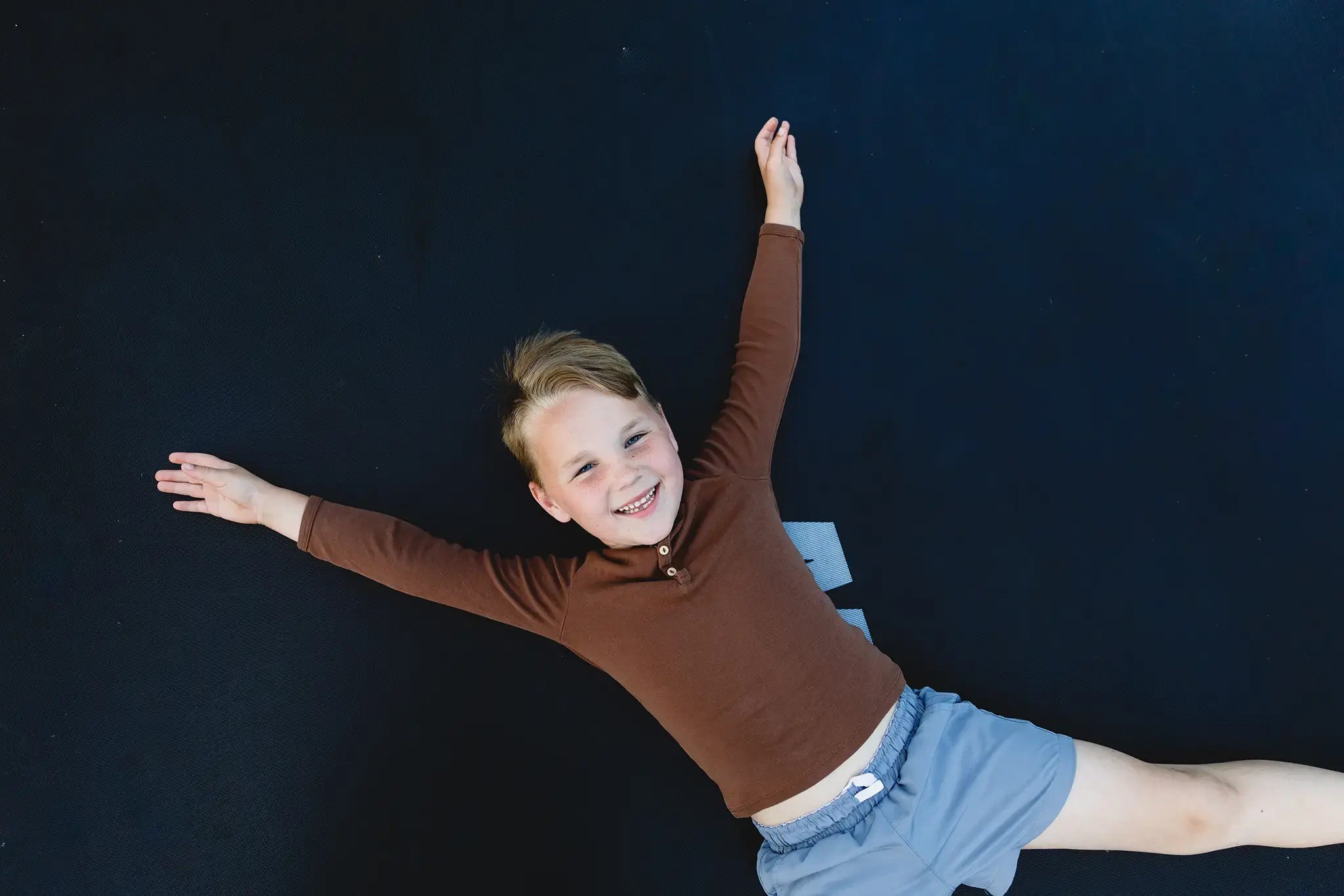 A happy child lying on a black Acon trampoline mat, arms spread wide.