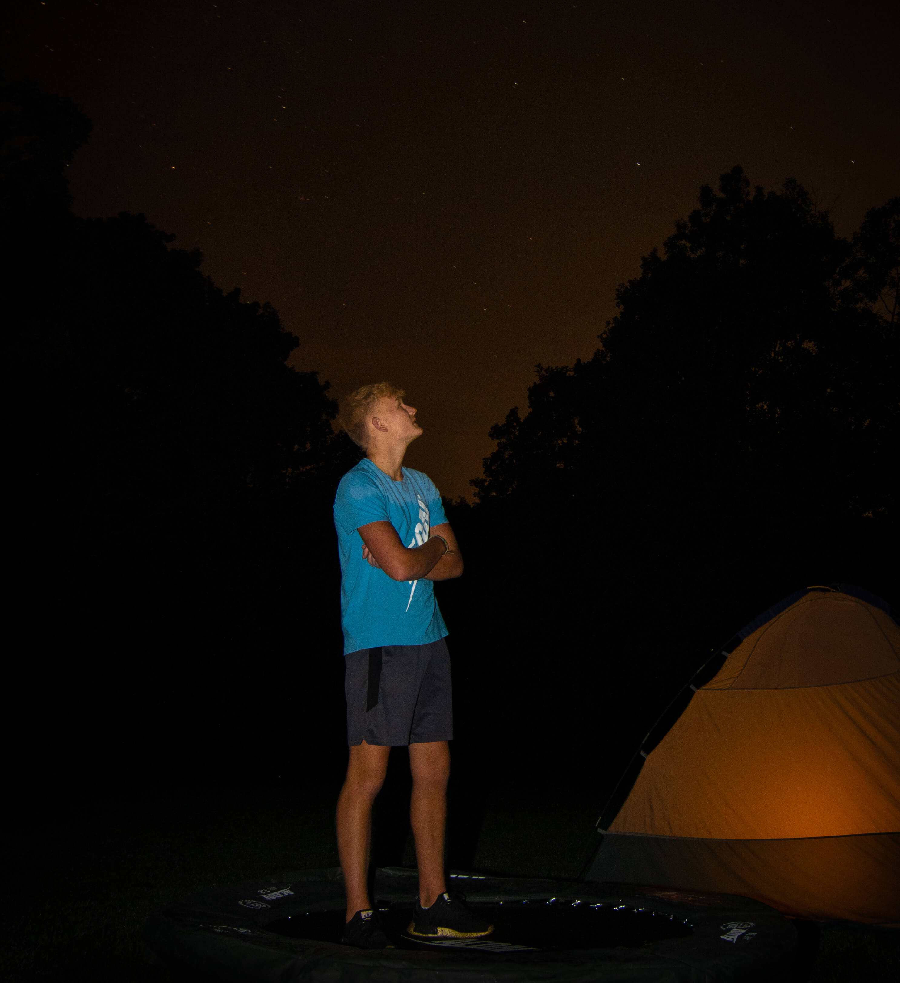 Boy standing on a trampoline and watching starry night sky.