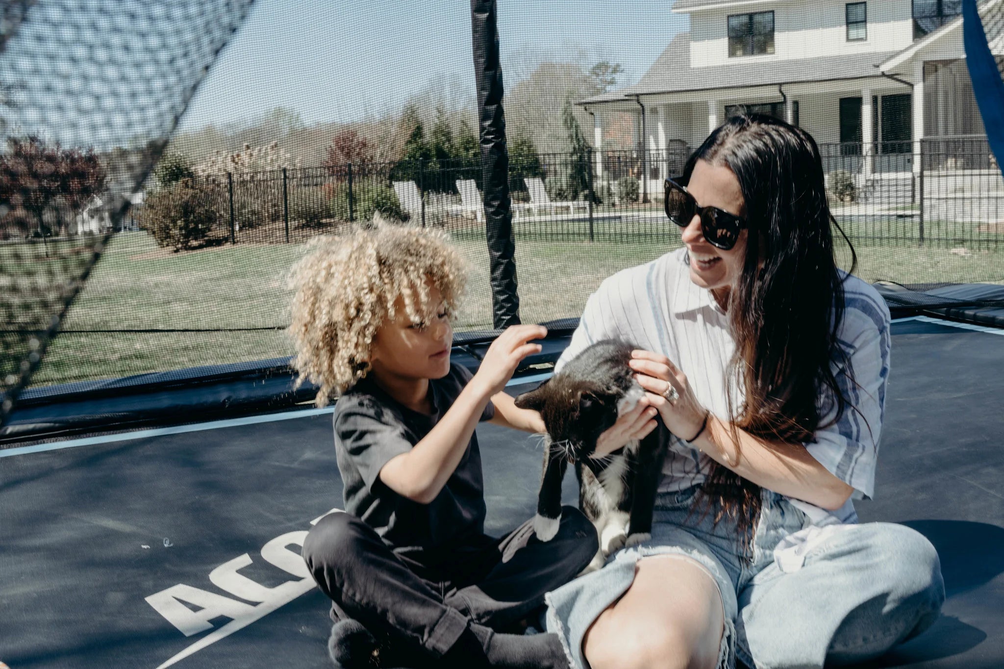 Child and mother on an Acon trampoline petting a cat.