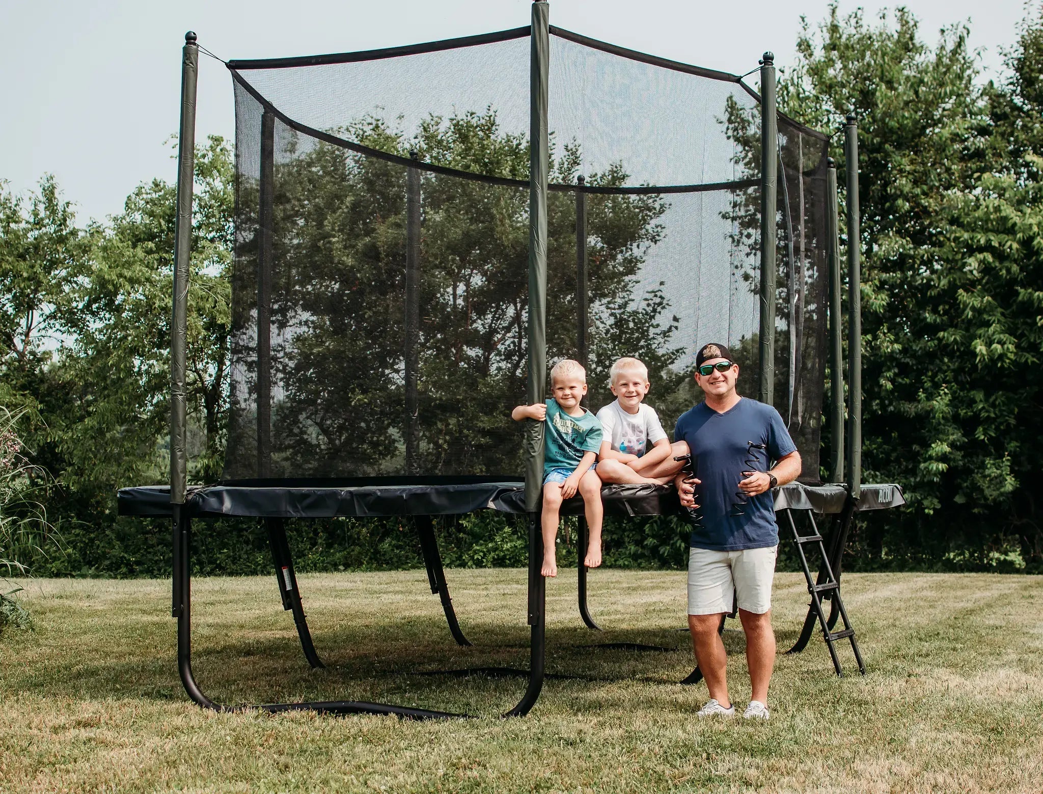A father and two children enjoying time near Acon trampoline on a sunny day.