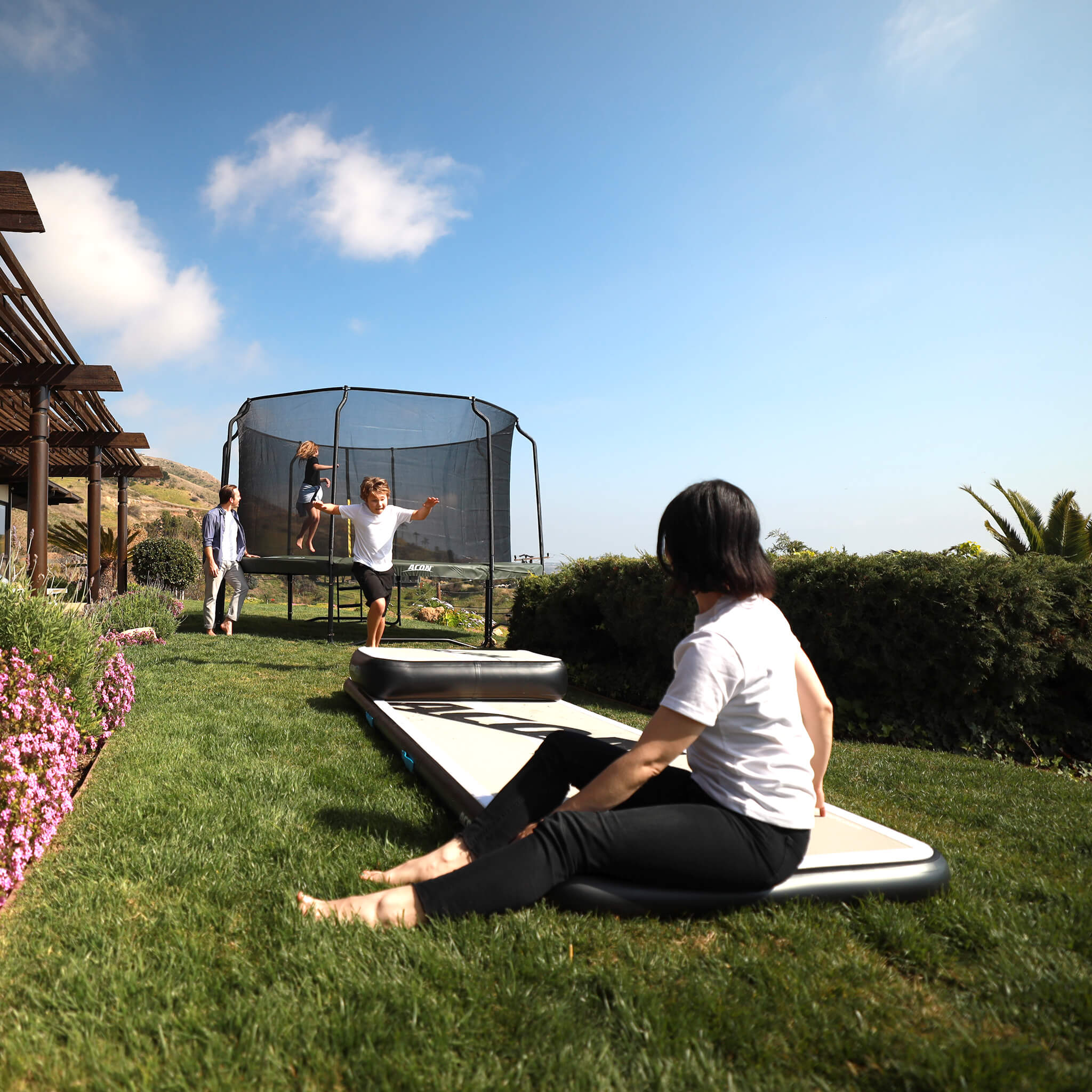 Family playing in the garden, girl jumping on a trampoline, boy running towards an airtrack