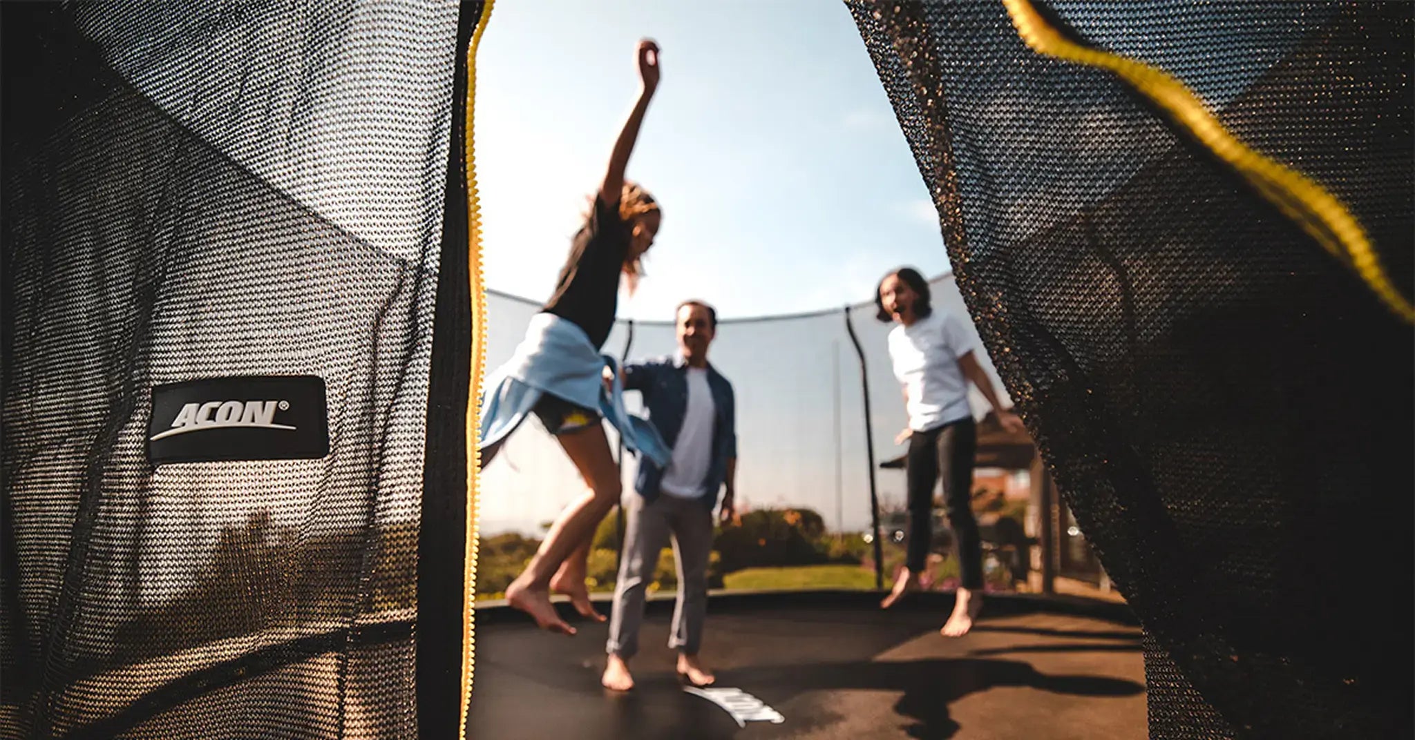 Family enjoying outdoor fun on an Acon trampoline, seen through the open safety net entrance.