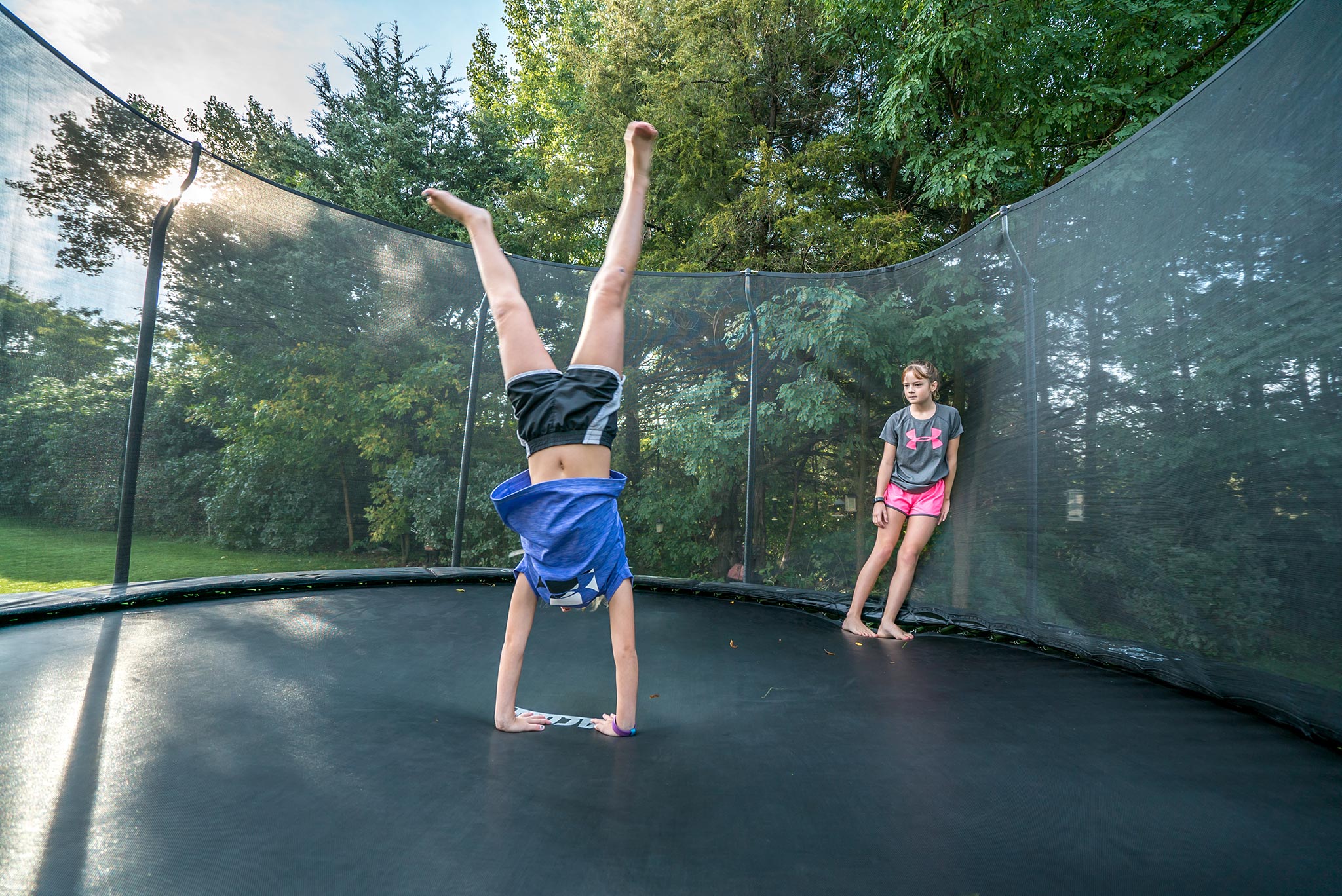 A girl handstanding a trampoline, fellow leaning to the safety net and watching