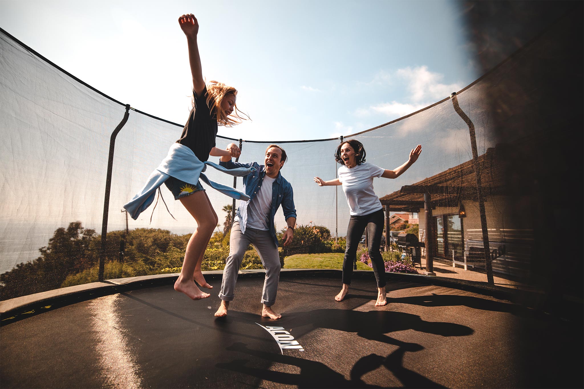 A girl on a round trampoline with her parents