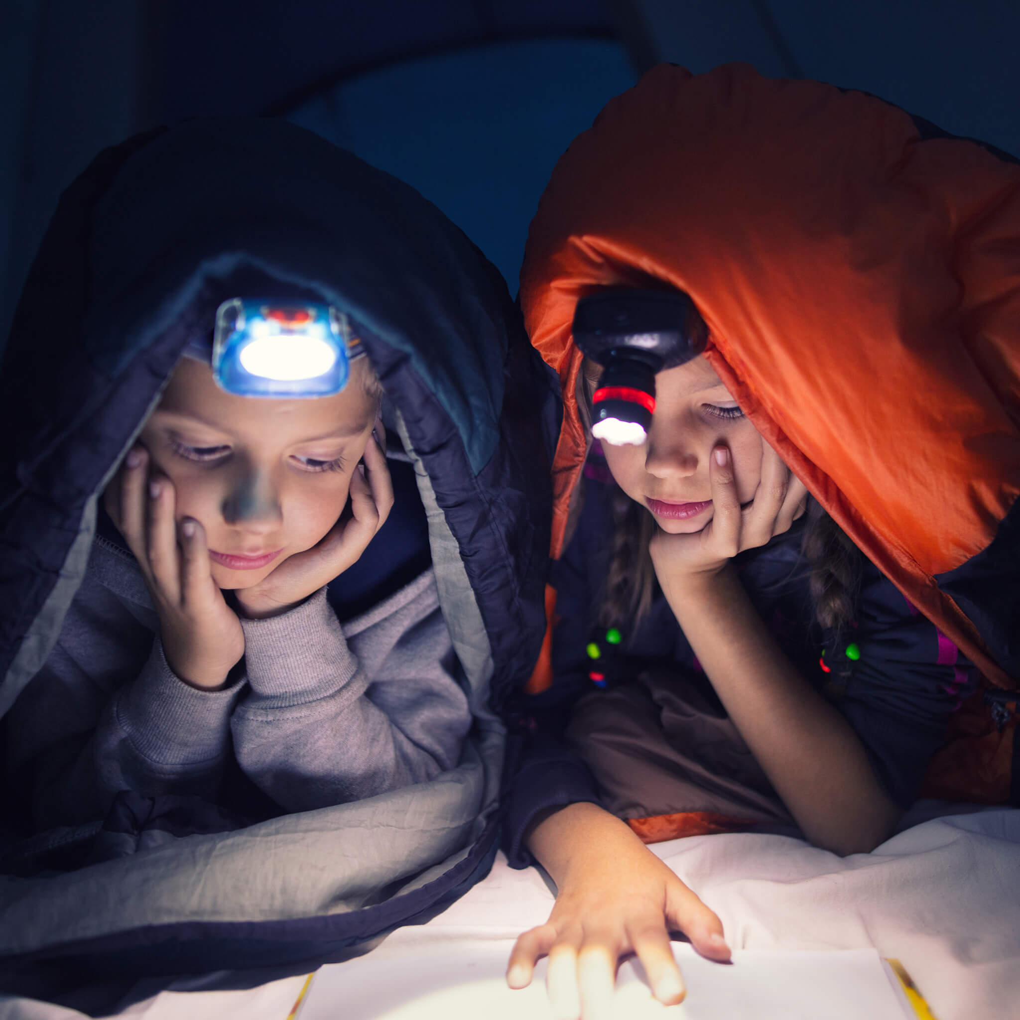 Girls wearing headlamps reading in a tent 