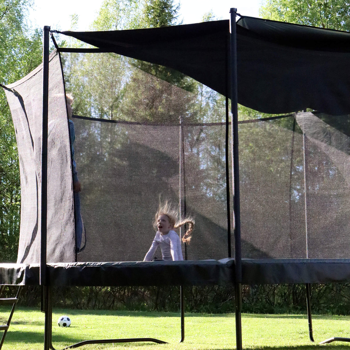 Half shade attached to a trampoline, with a child jumping underneath.