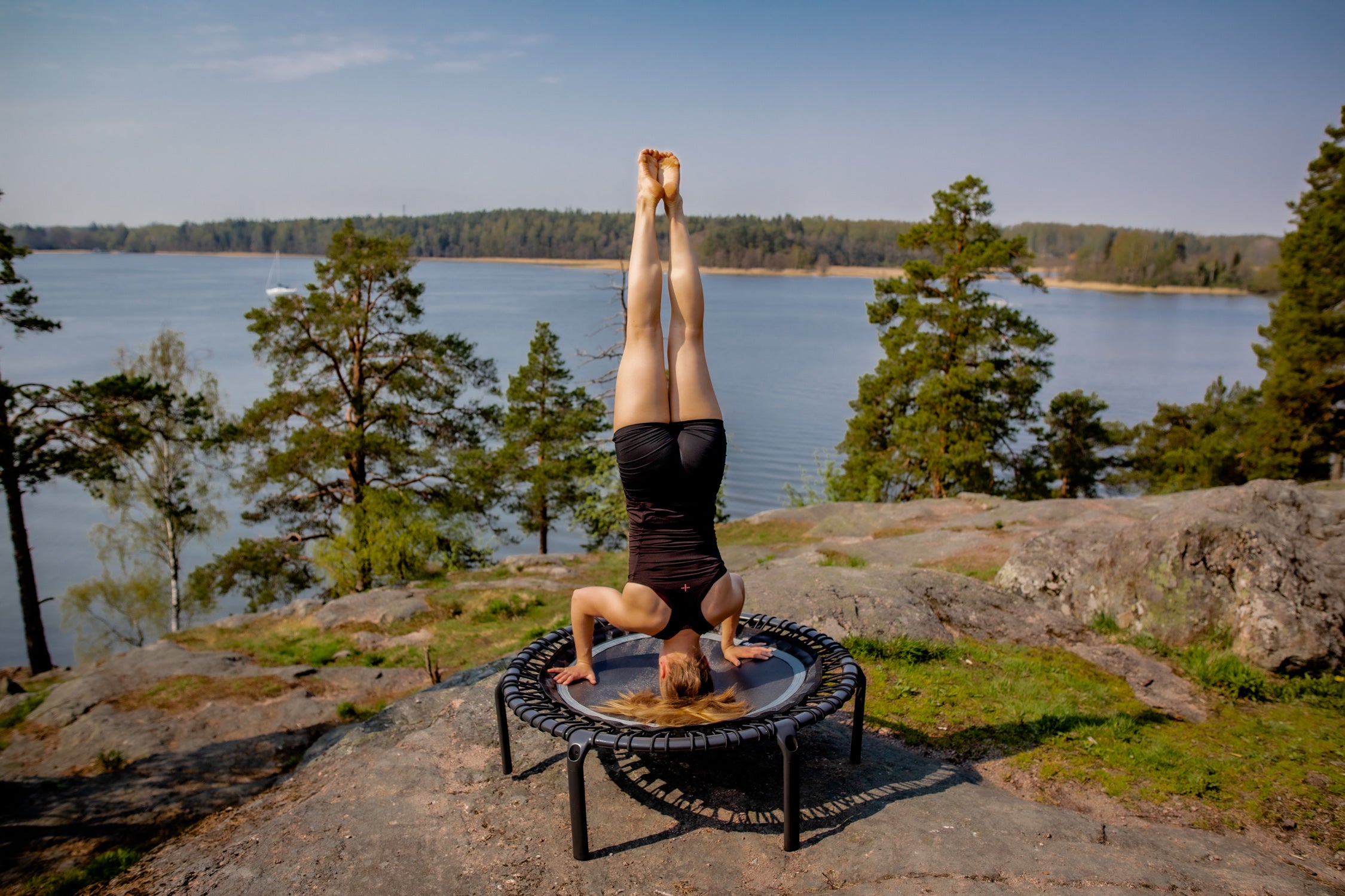 A woman doing a headstand on a mini fitness trampoline outdoors in the forest