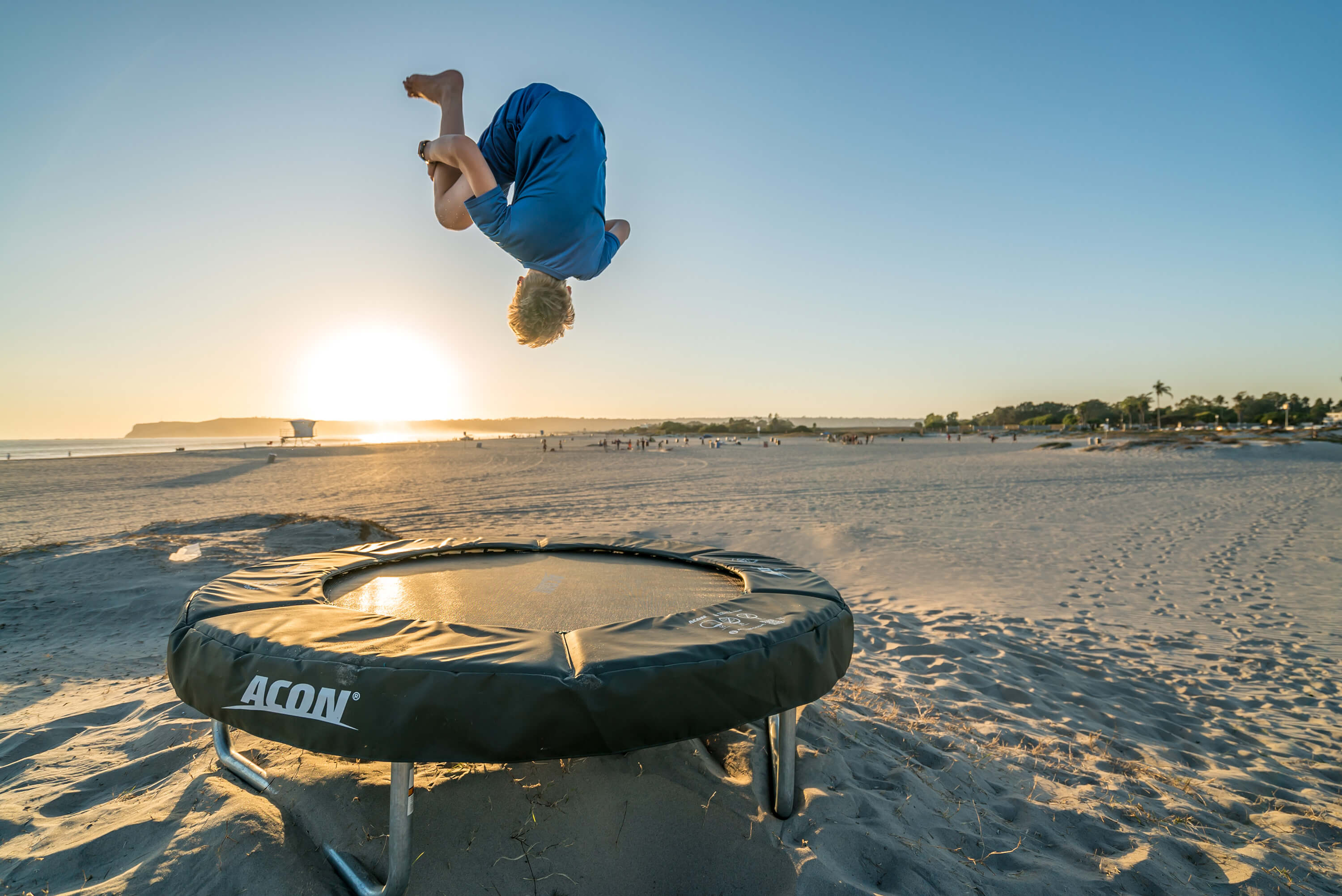 A boy jumping on a trampoline in a seaside landscape.