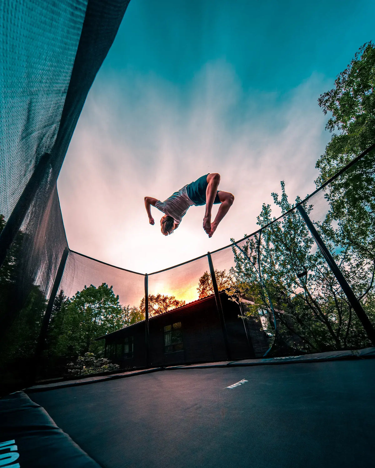 Person performing a flip on an ACON trampoline at sunset.